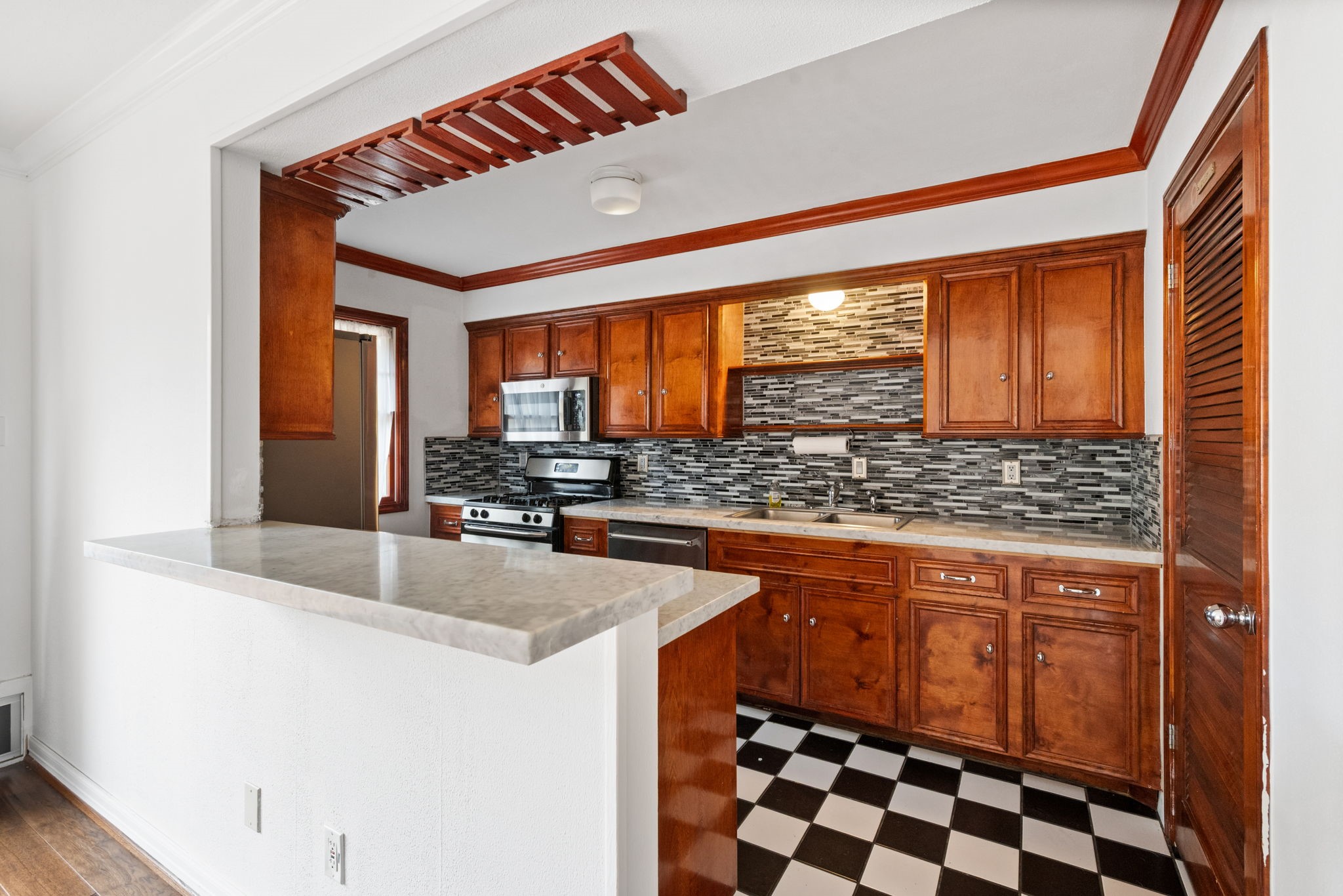 Charming kitchen featuring warm wooden cabinetry, modern stainless steel appliances, and a stylish mosaic backsplash, complemented by a classic black-and-white checkered floor.