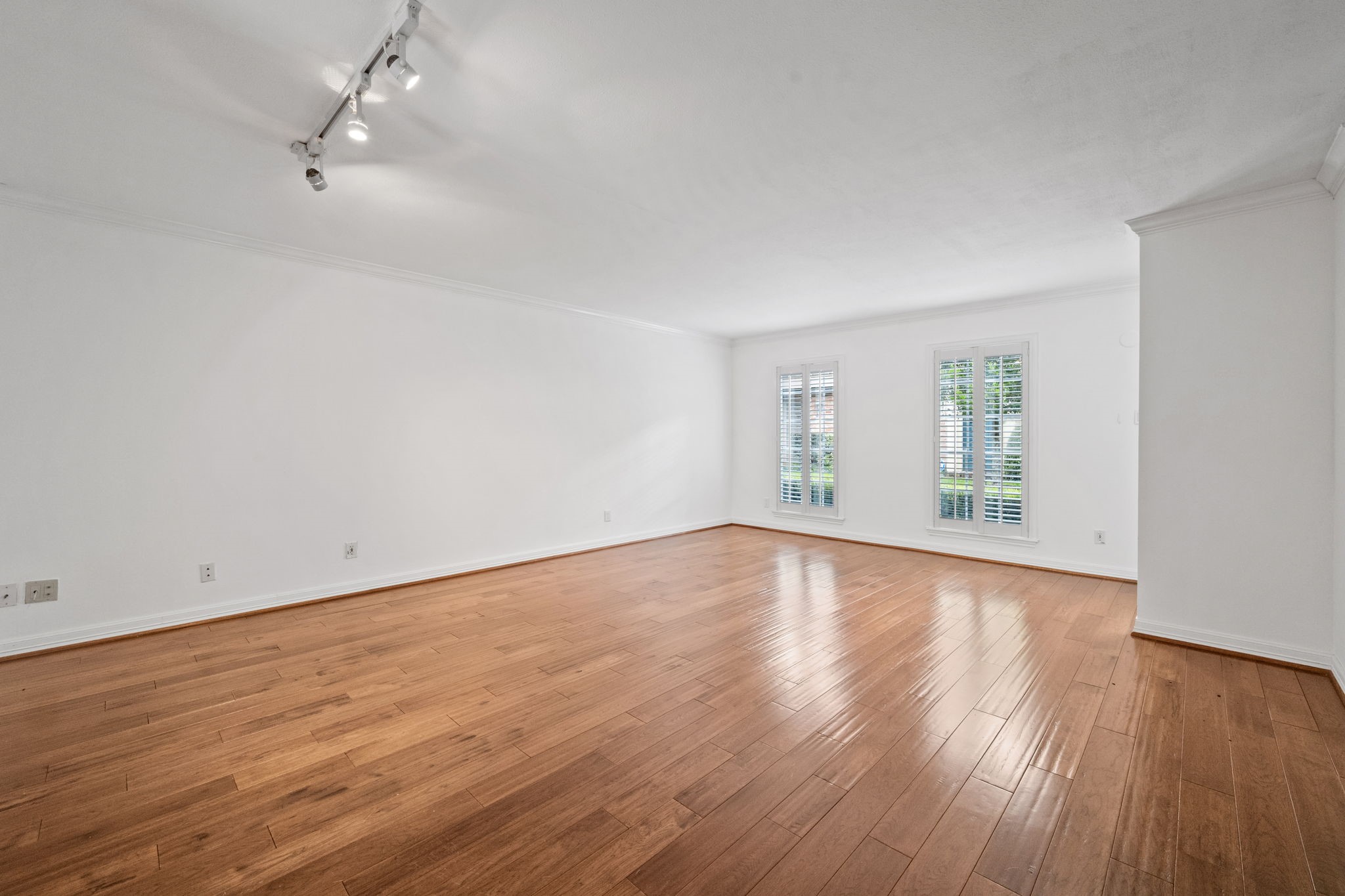 Spacious, light-filled living area with sleek hardwood floors and large windows adorned with elegant shutters, perfect for modern living. Spacious, light-filled living area with sleek hardwood floors and large windows adorned with elegant shutters, perfect for modern living.