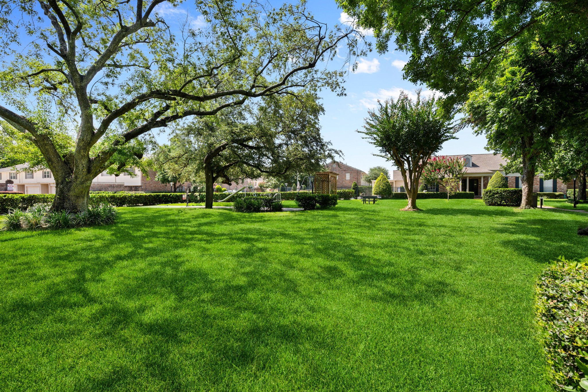 Expansive, lush green lawn shaded by mature trees, perfect for outdoor relaxation and gatherings, with charming homes in the background.