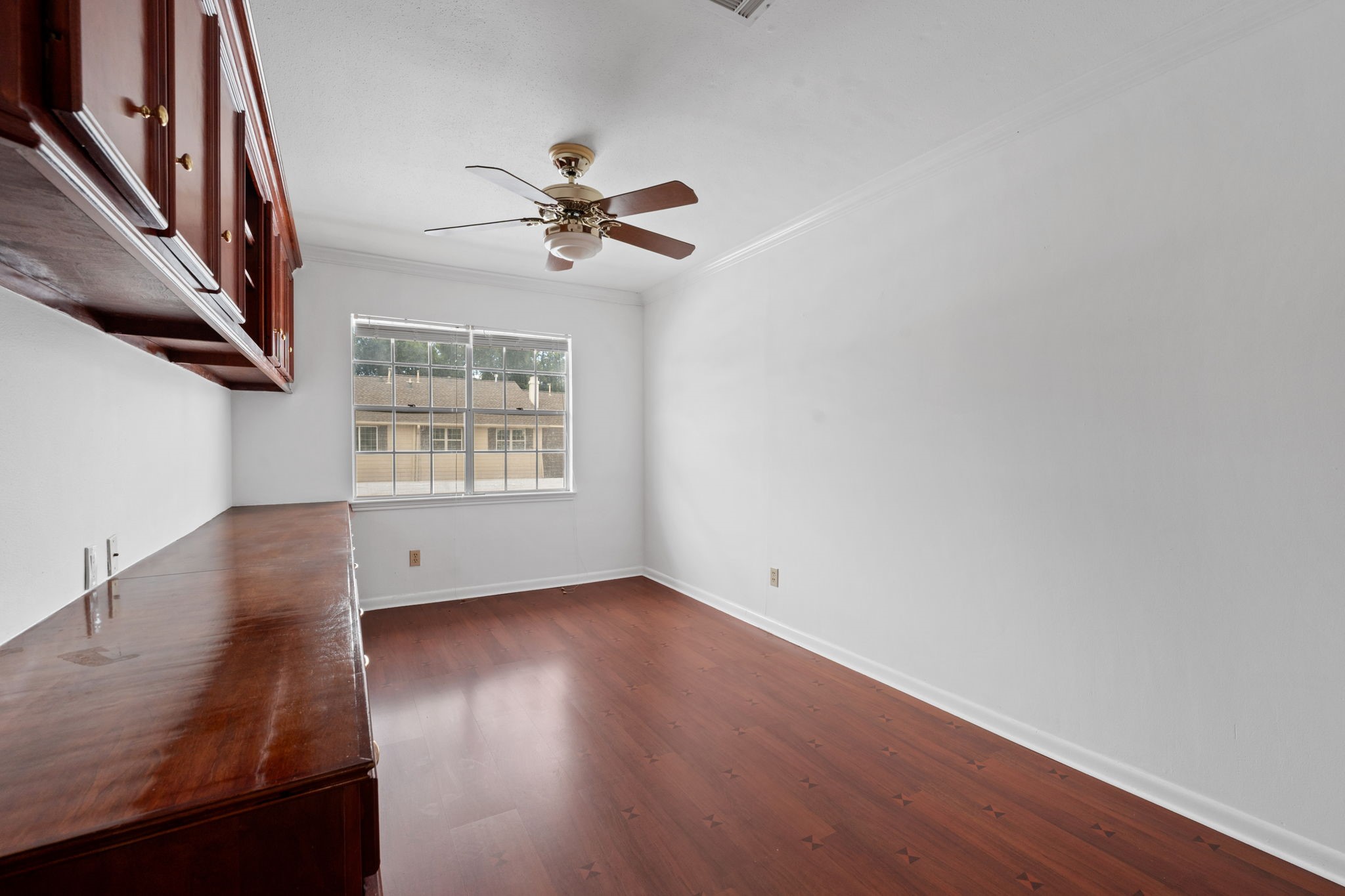 Bright room with elegant wood flooring, built-in cabinetry, and a ceiling fan, offering a cozy and functional space.