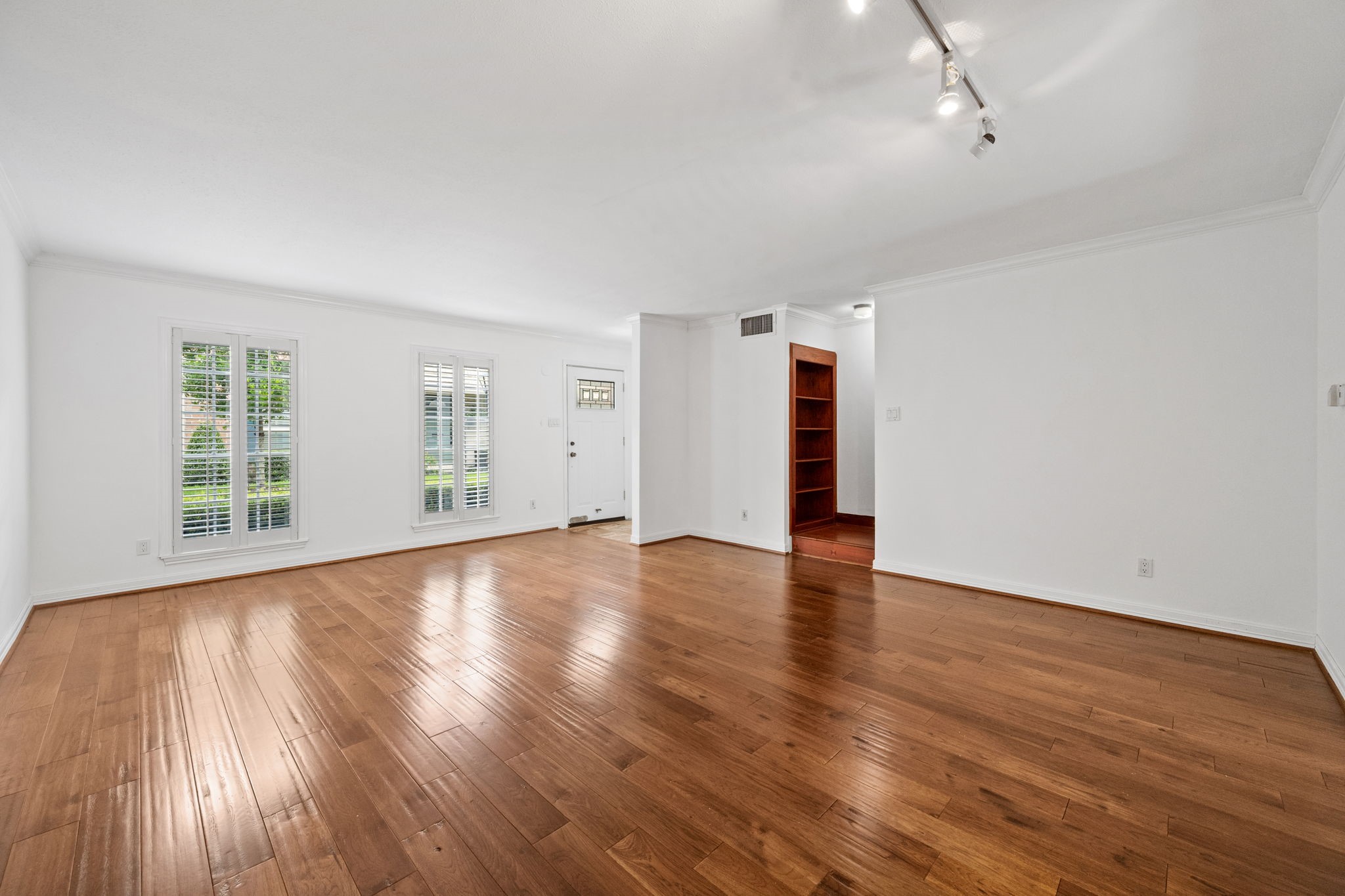 Spacious living area with gleaming hardwood floors, abundant natural light from large windows, and modern track lighting. Spacious living area with gleaming hardwood floors, abundant natural light from large windows, and modern track lighting.