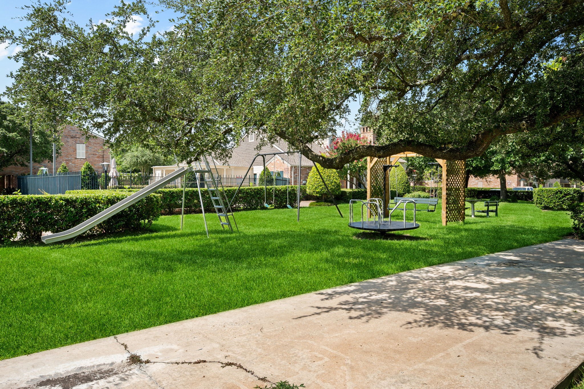 Charming backyard oasis featuring a well-maintained playground with a slide and merry-go-round, surrounded by lush greenery and mature trees, perfect for family fun.