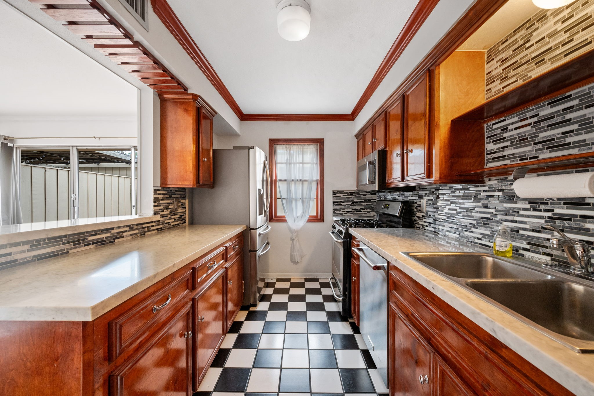 Charming kitchen with rich wooden cabinetry and sleek modern backsplash, complemented by a classic black-and-white checkered floor.
