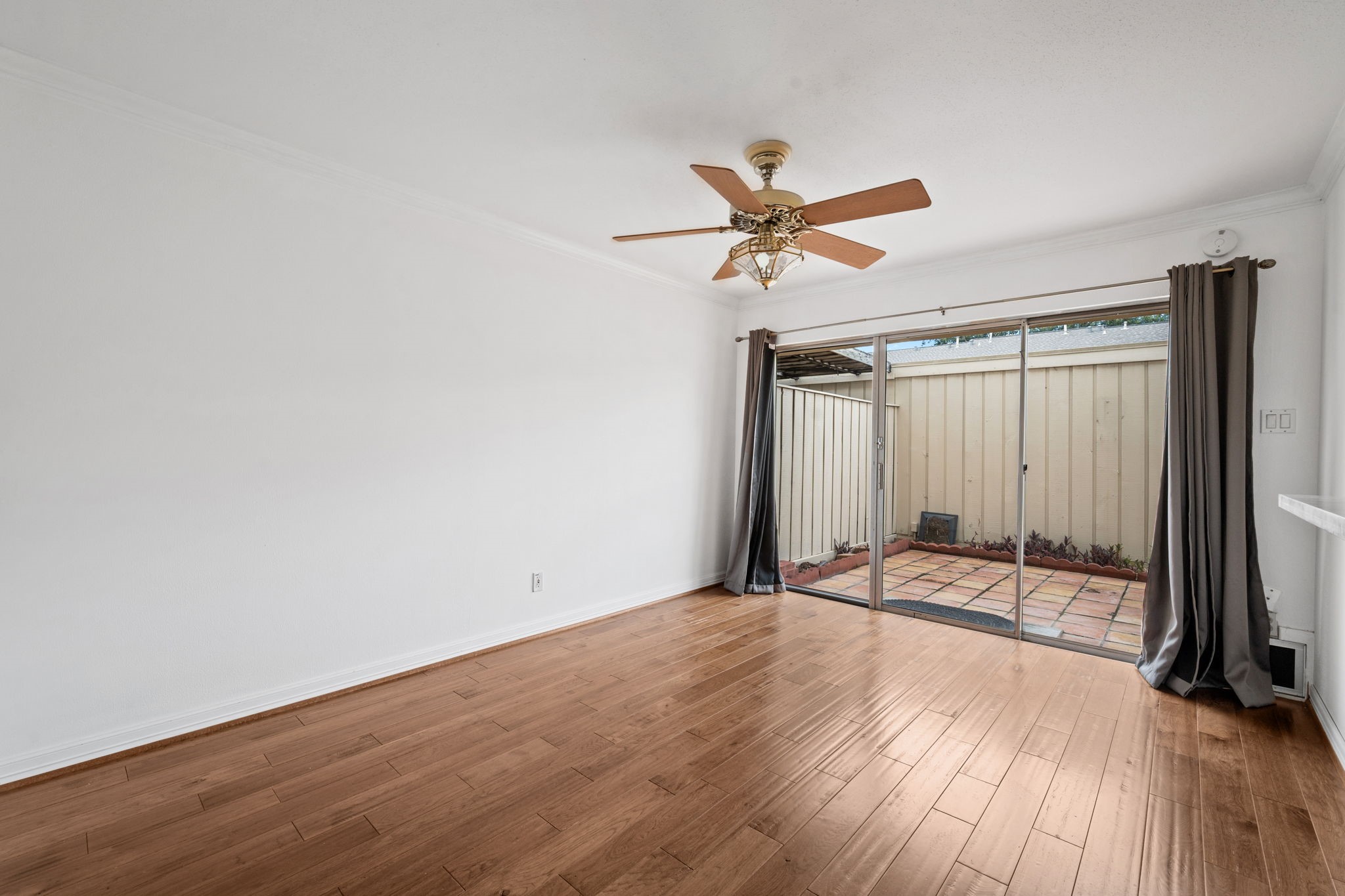 Bright and inviting room featuring elegant hardwood floors, a stylish ceiling fan, and sliding glass doors leading to a charming patio. Bright and inviting room featuring elegant hardwood floors, a stylish ceiling fan, and sliding glass doors leading to a charming patio.