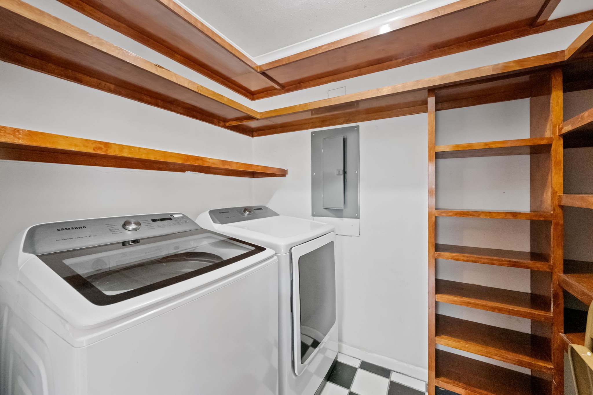 Spacious laundry room featuring modern appliances, ample wooden shelving, and a stylish checkerboard floor.