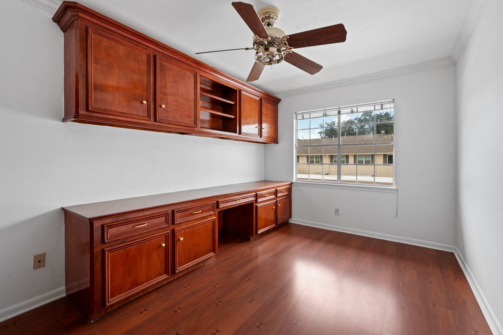 Spacious room featuring elegant wood cabinetry and a ceiling fan, complemented by natural light from a large window. Perfect for a home office or study.