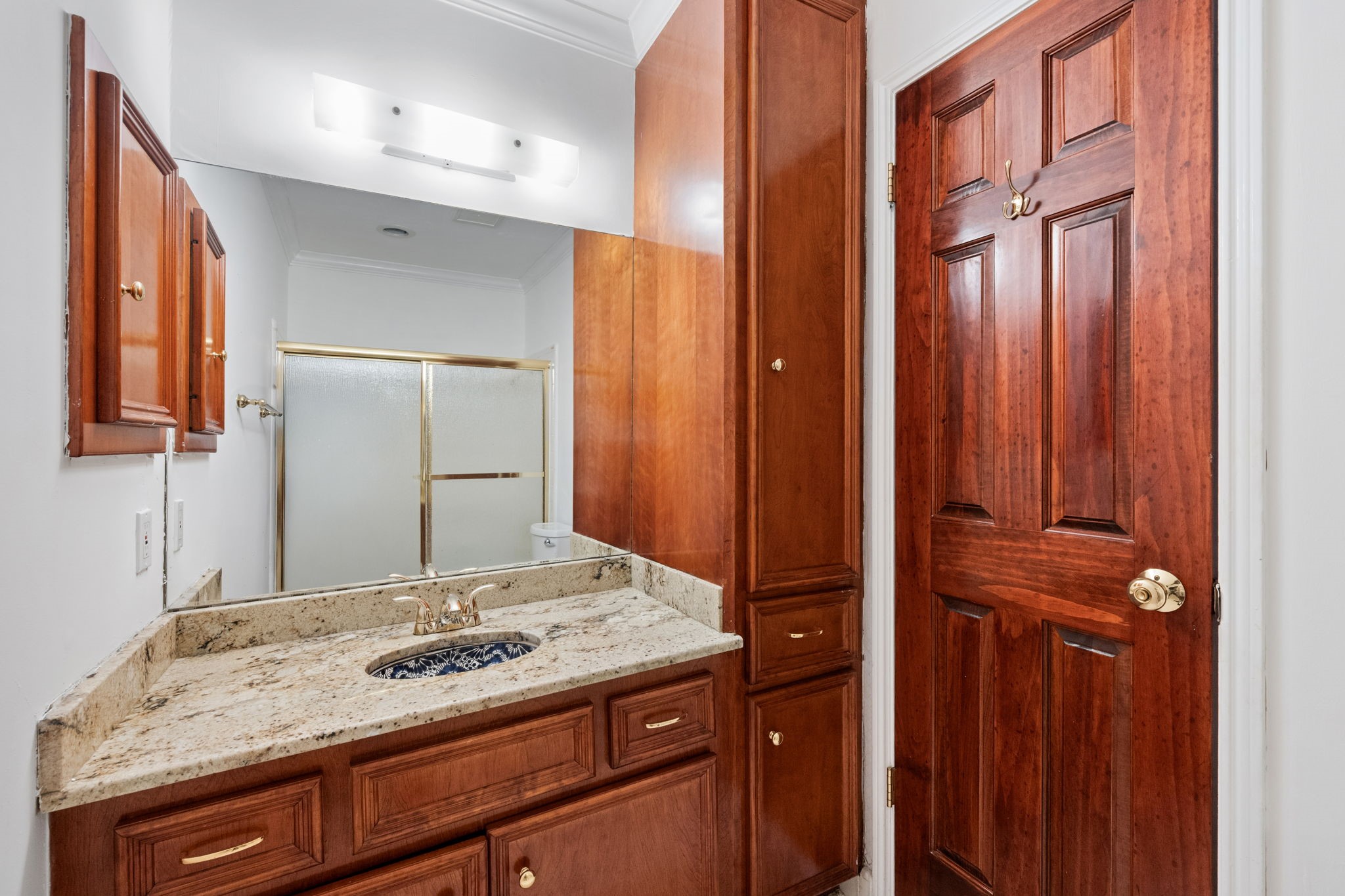 Elegant bathroom features rich wood cabinetry, a sleek granite countertop, and a stylish glass-enclosed shower.