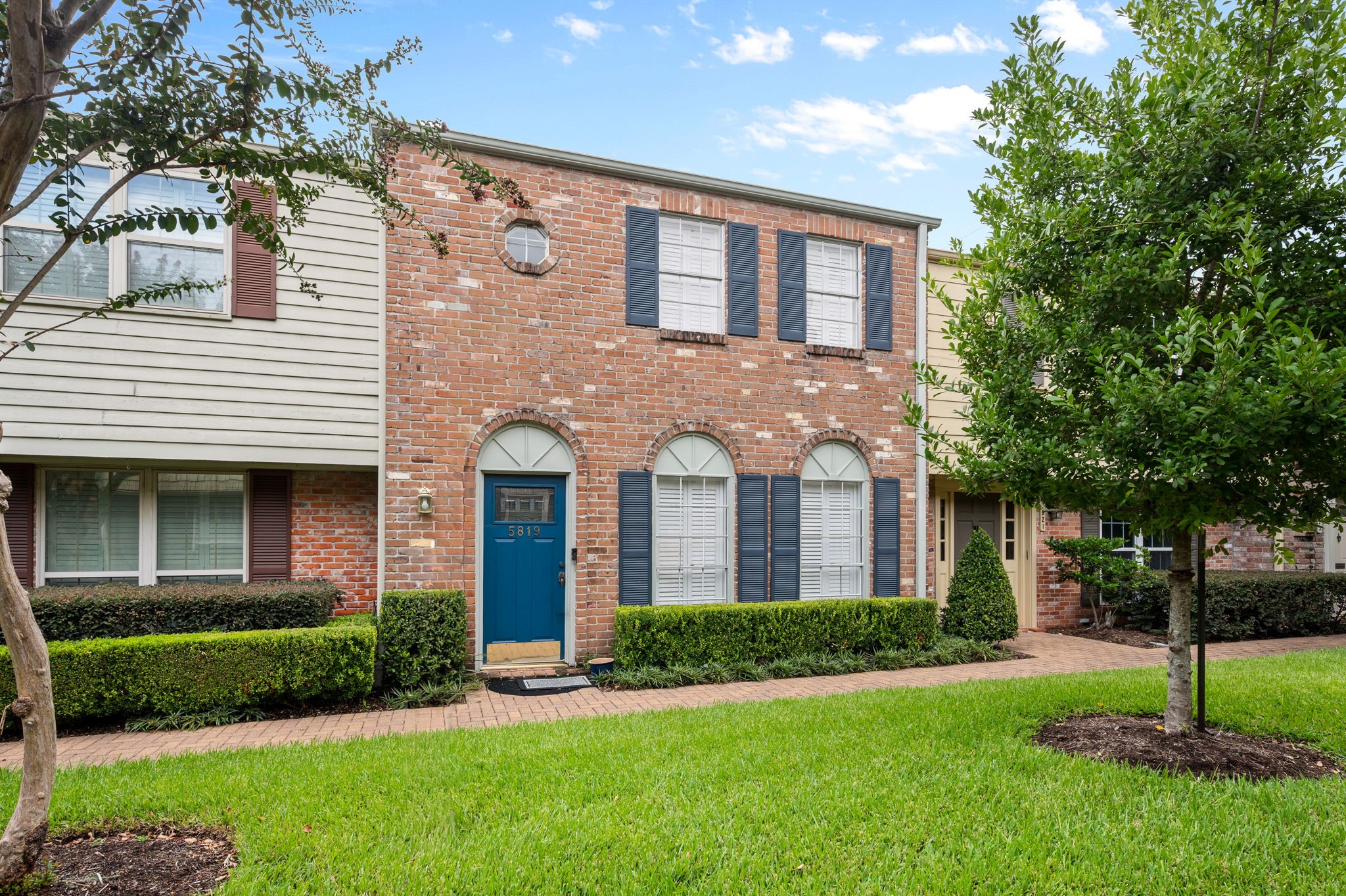 Charming brick townhouse with elegant shutters, arched windows, and a vibrant blue front door, nestled in a well-maintained neighborhood with lush greenery. Charming brick townhouse with elegant shutters, arched windows, and a vibrant blue front door, nestled in a well-maintained neighborhood with lush greenery.