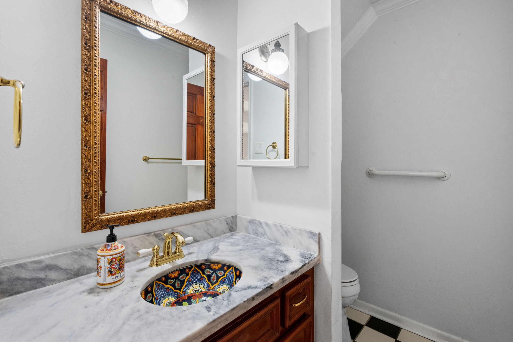 Elegant bathroom featuring a marble countertop with a colorful mosaic sink, ornate gold-framed mirror, and classic black-and-white checkered flooring.