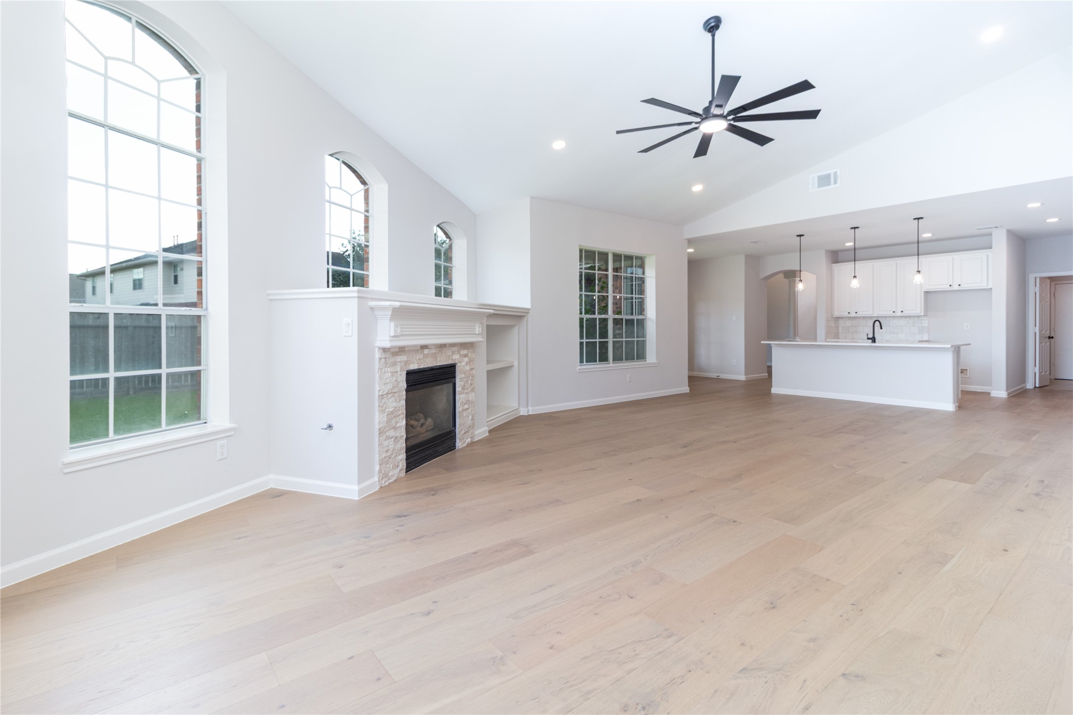 Living room looking back towards the gas fireplace and kitchen area. High ceiling, new engineered wood flooring, fixtures, and new paint.