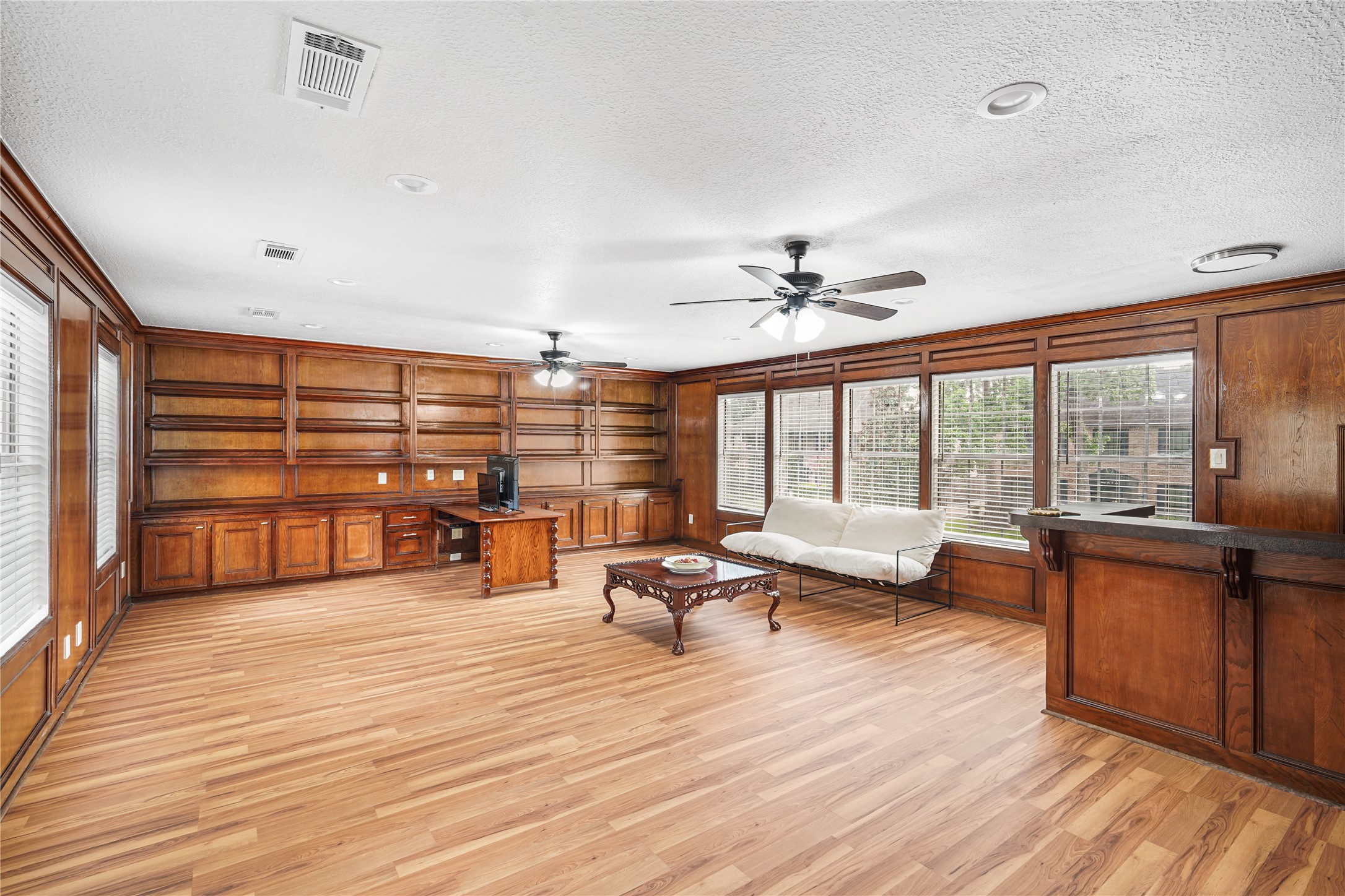 Upstairs gameroom area with rich wood paneling, built-in shelving, a wet bar, and large windows offering ample natural light.