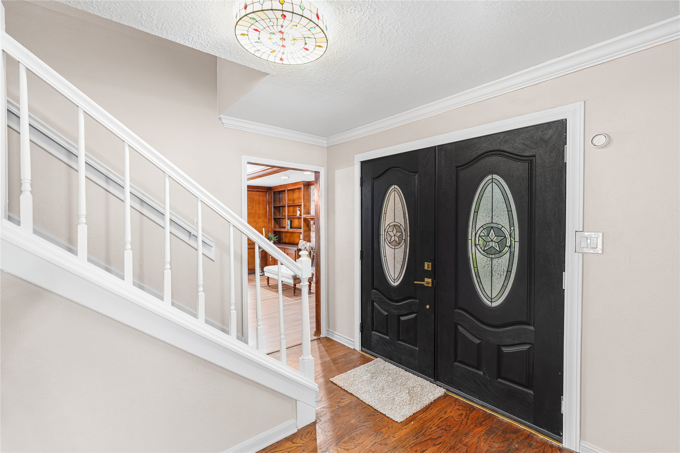 Elegant entryway featuring striking double doors with decorative glass, complemented by a stylish staircase and warm wood flooring.