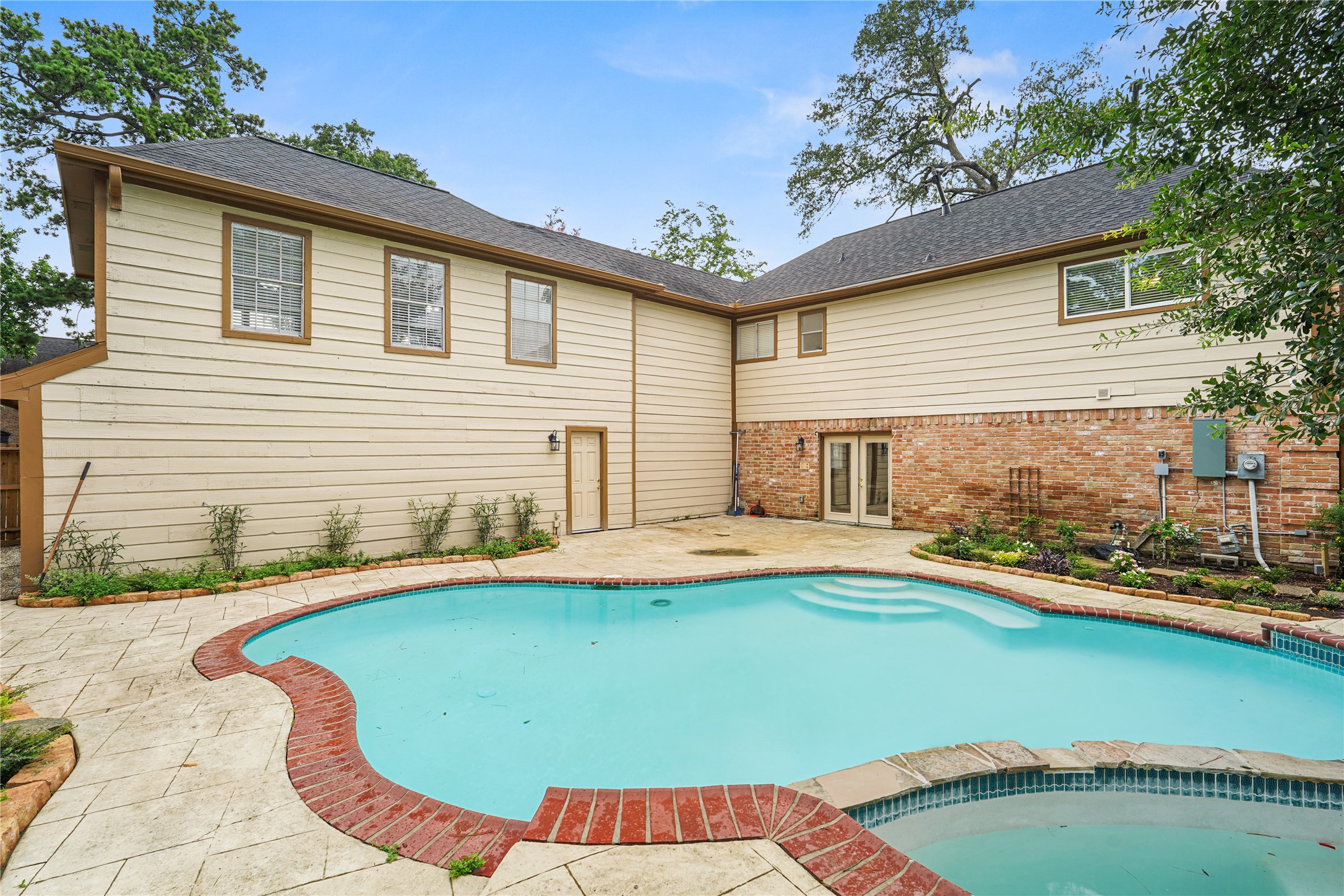 Spacious backyard featuring a beautifully curved pool surrounded by a stone patio, perfect for outdoor relaxation and entertaining.