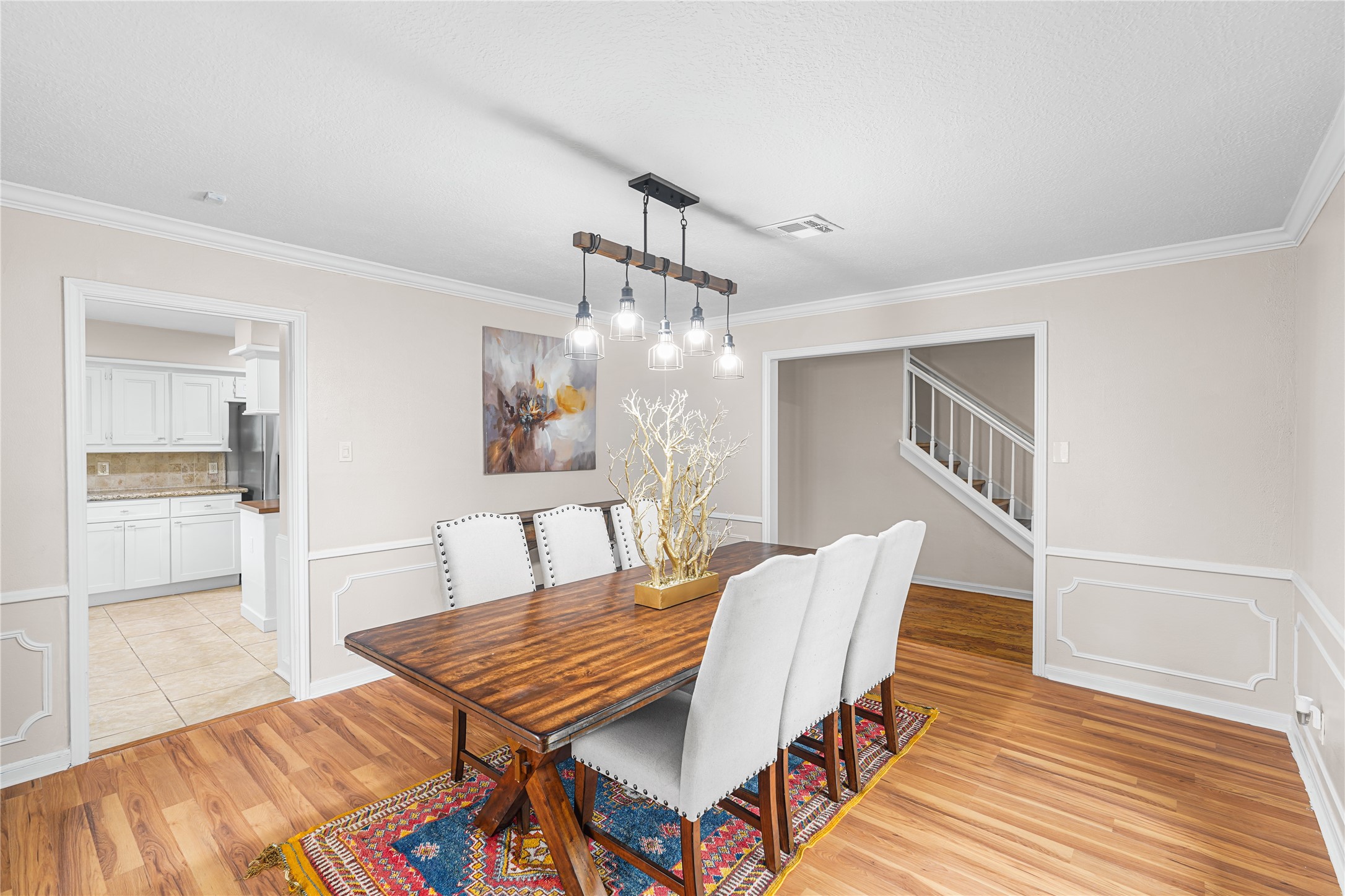 Elegant dining room with hardwood floors and stylish pendant lighting. The space opens to a bright kitchen.