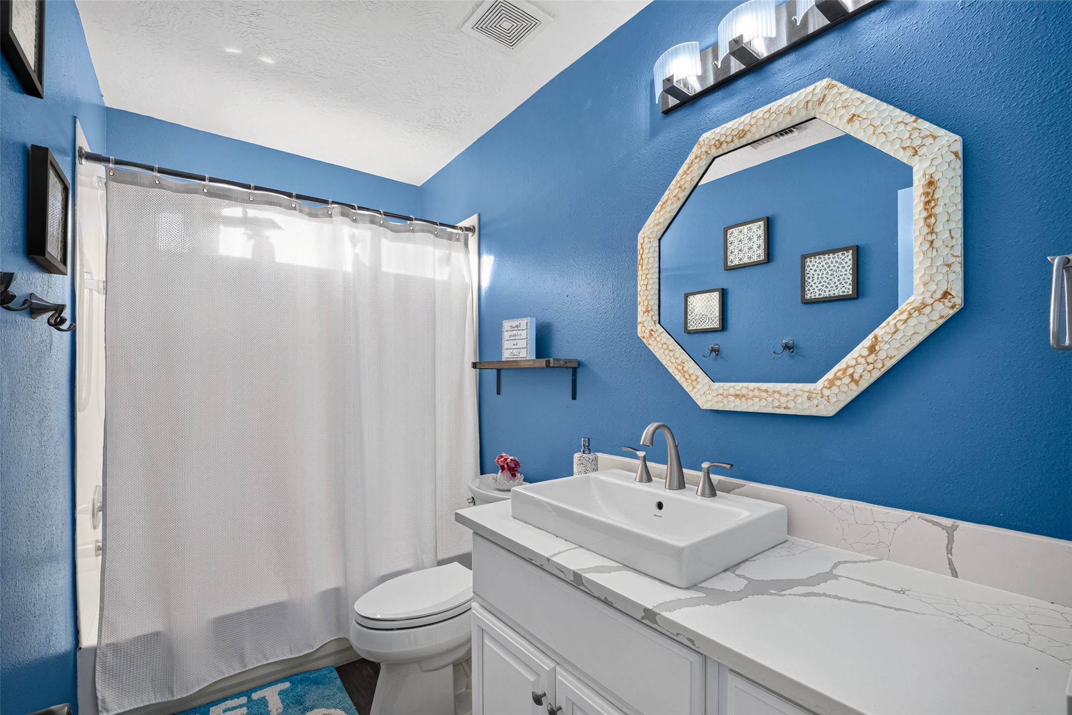 Full bath with blue walls and a stylish octagonal mirror.