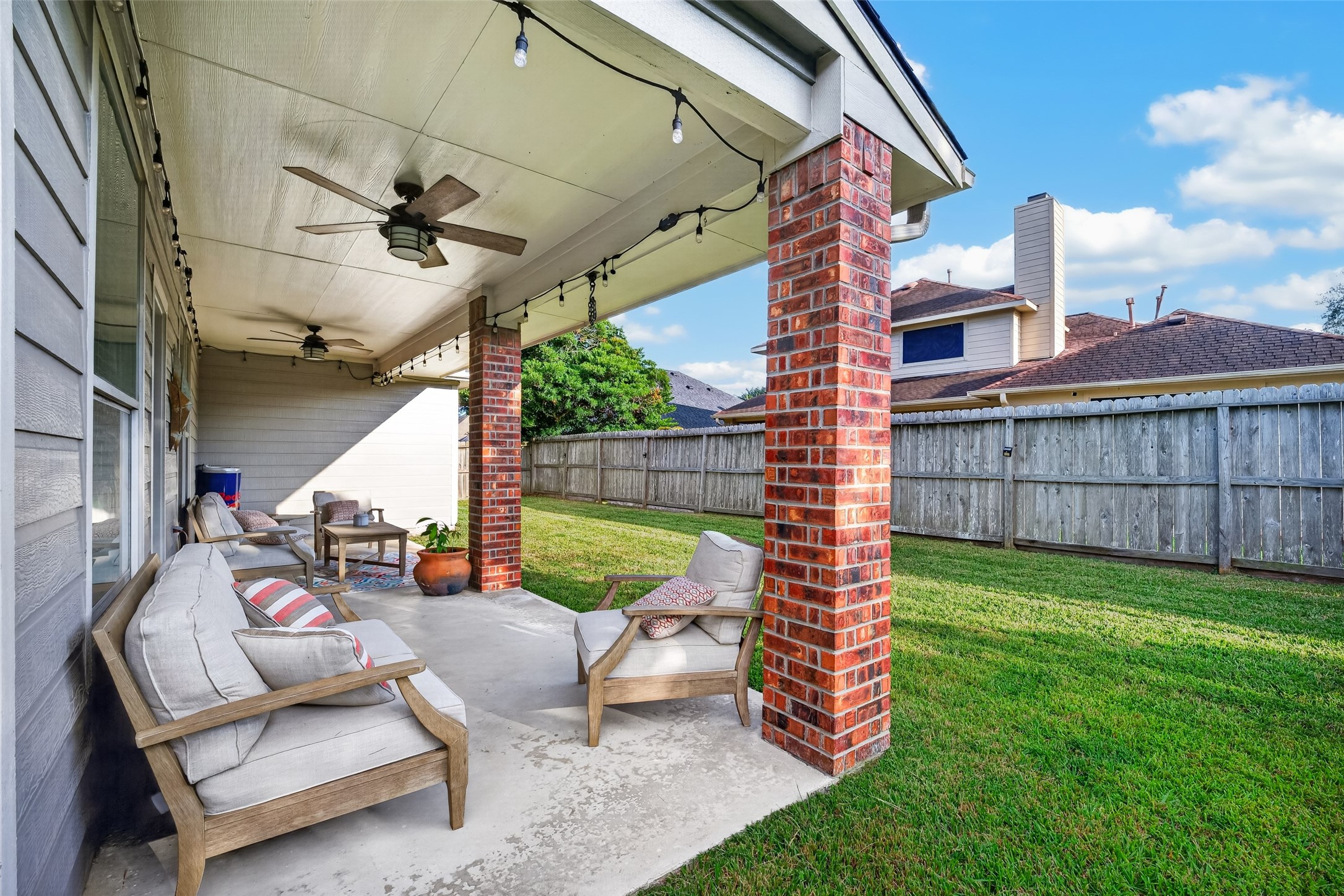 Fenced backyard with patio seating and green lawn.