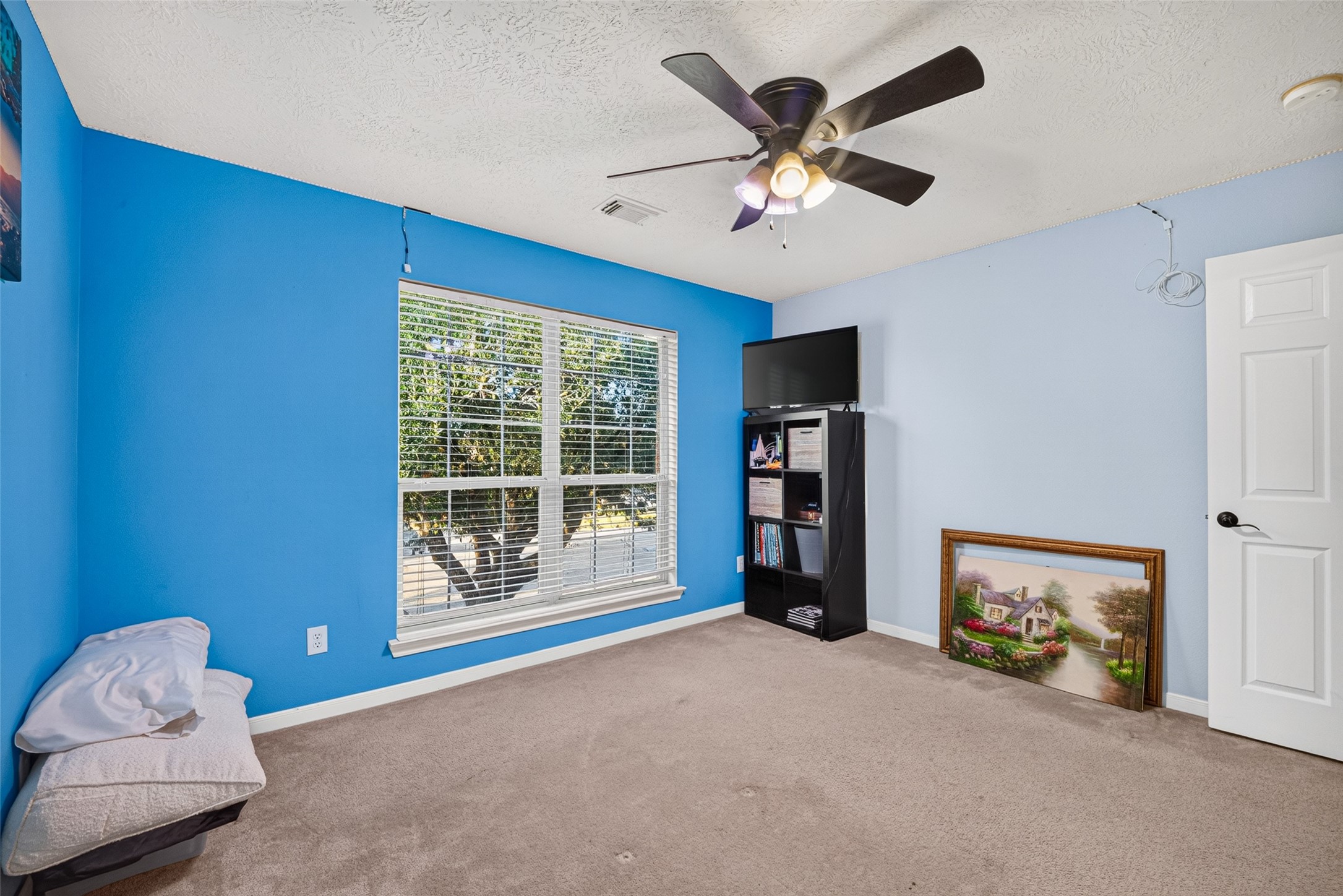 Cheerful bedroom with blue accent wall and big bright windows.