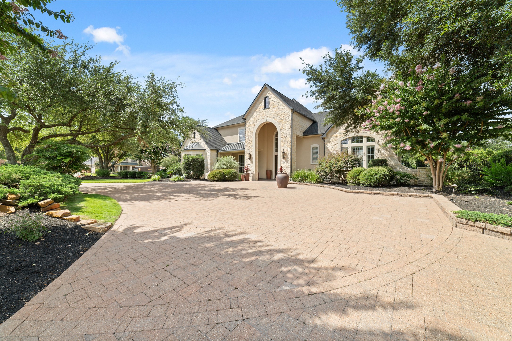 This stunning home features a grand entrance with a spacious, landscaped driveway surrounded by lush greenery and mature trees. The elegant architecture and well-maintained exterior create a welcoming and luxurious curb appeal.