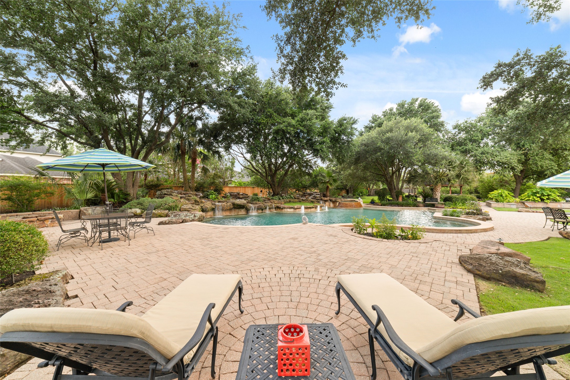 This backyard oasis features a spacious patio surrounded by lush greenery and mature trees, perfect for relaxation and entertaining.