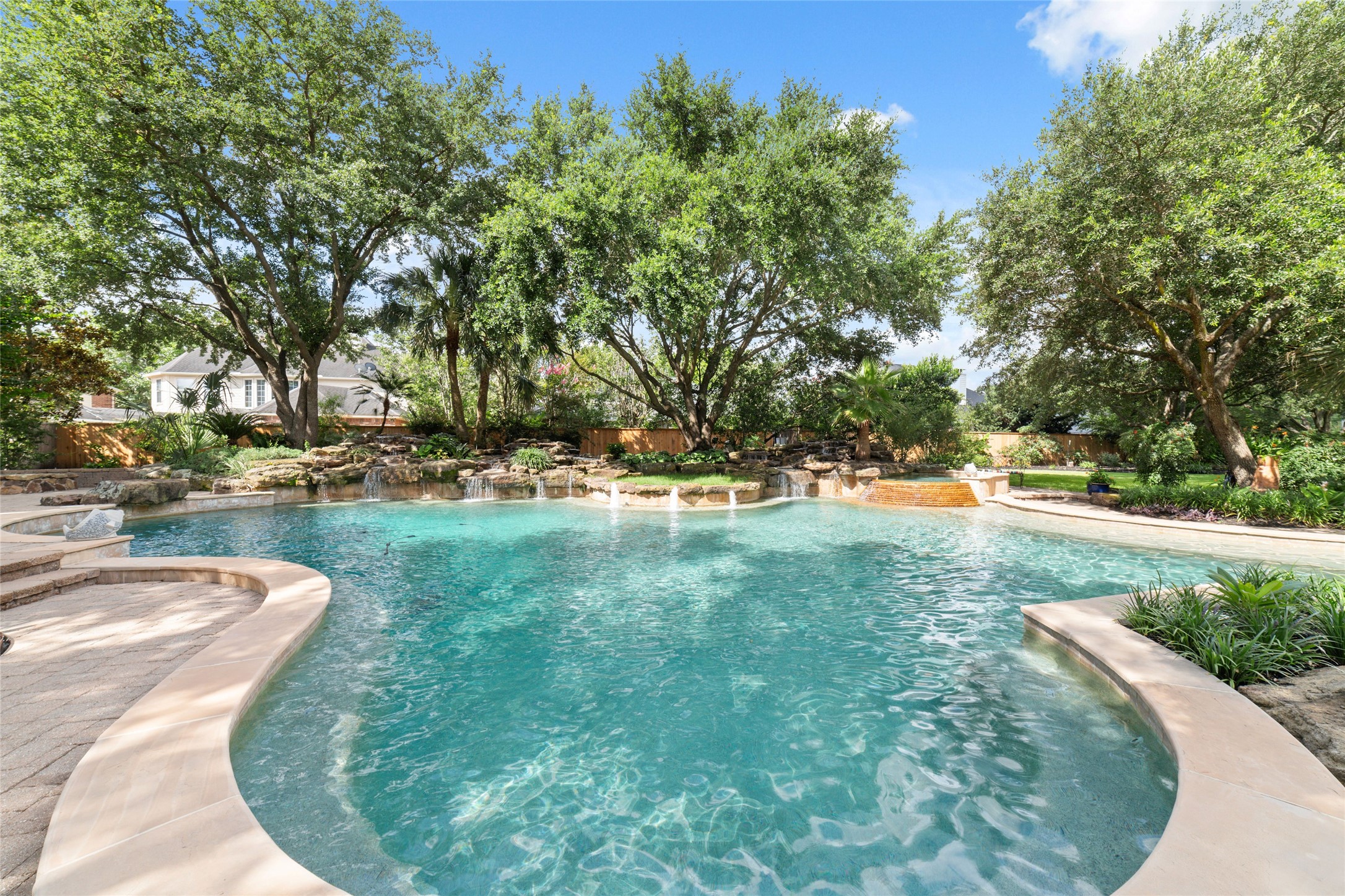This serene backyard features a large, inviting pool with a waterfalls, offering a private oasis perfect for relaxation and entertaining.