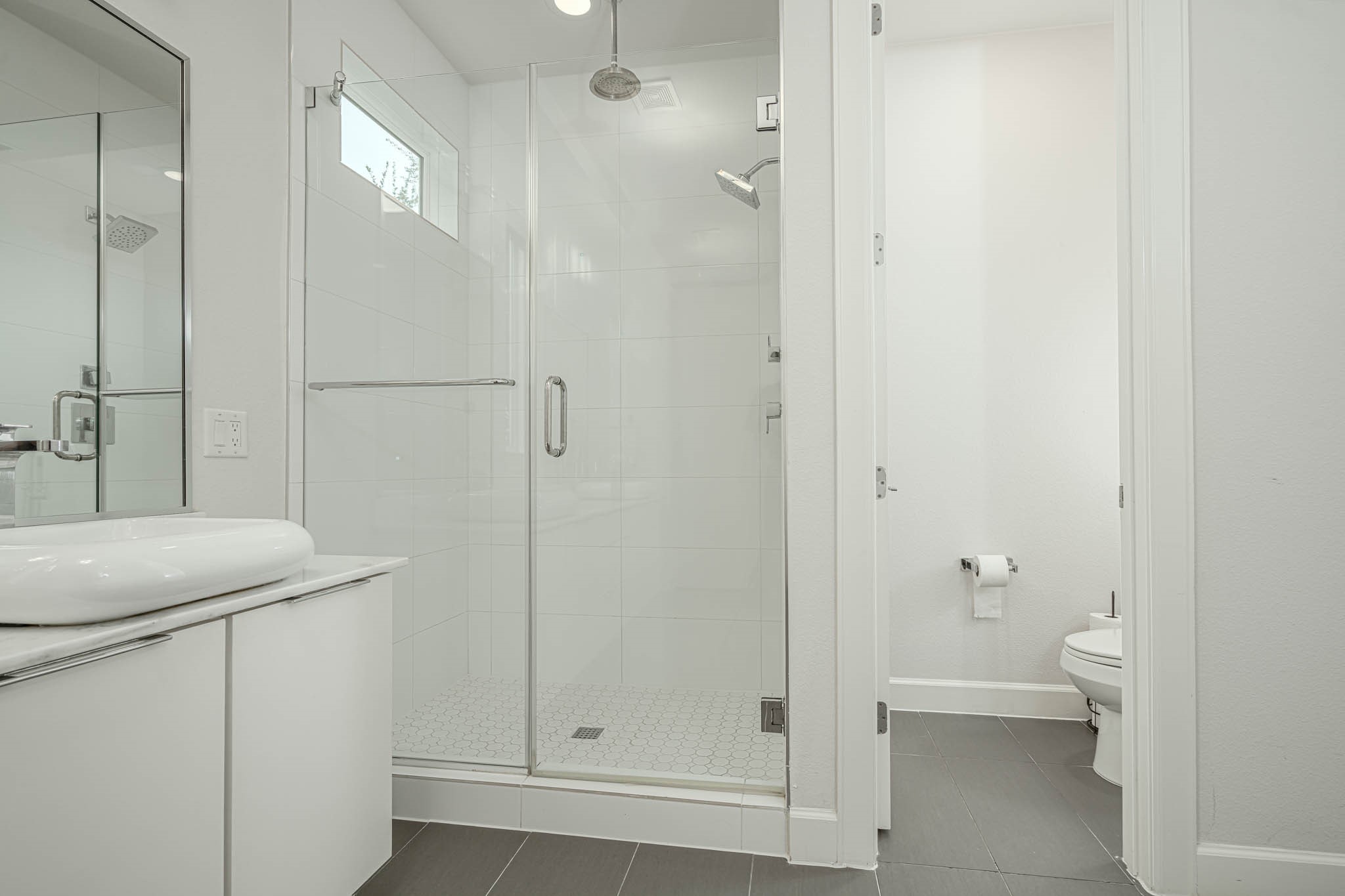 Sleek and modern bathroom featuring a spacious glass-enclosed shower, elegant vanity, and a separate toilet area for added privacy.