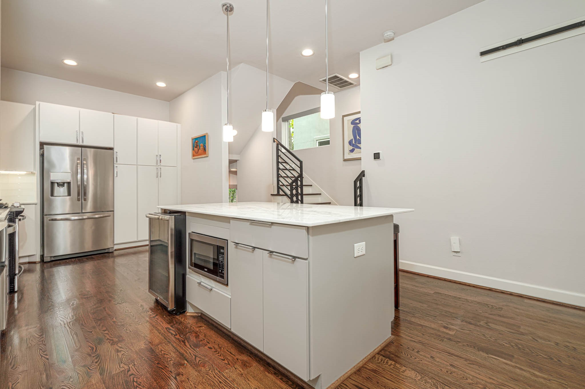 Modern kitchen featuring sleek stainless steel appliances, a spacious island with built-in microwave, and elegant hardwood floors, all accented by stylish pendant lighting.