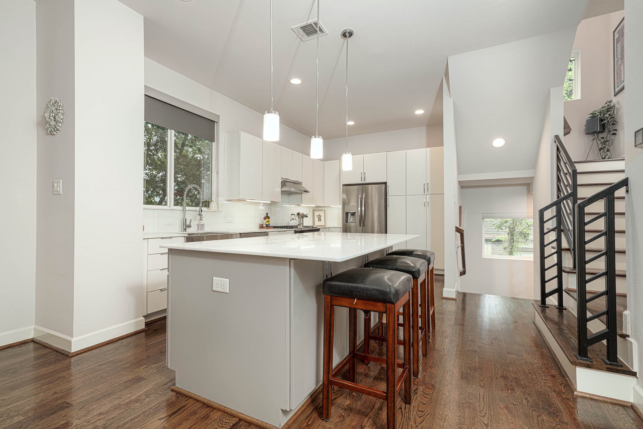 Modern kitchen with sleek white cabinetry, stainless steel appliances, and a large island with bar seating, complemented by warm hardwood floors and recessed lighting.