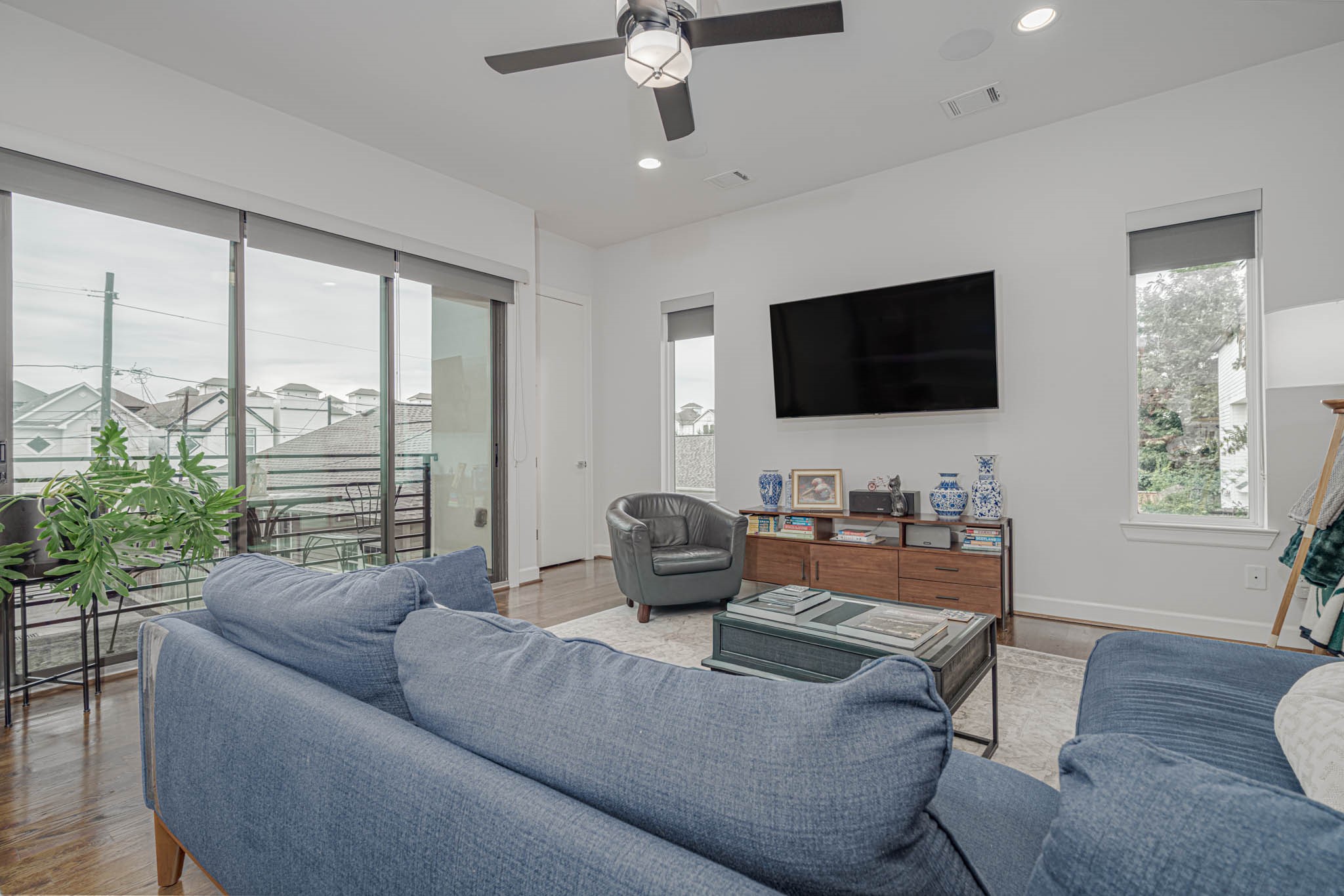 Bright and inviting living area with a modern ceiling fan, large windows offering natural light, and a cozy seating arrangement, perfect for relaxation and entertainment.
