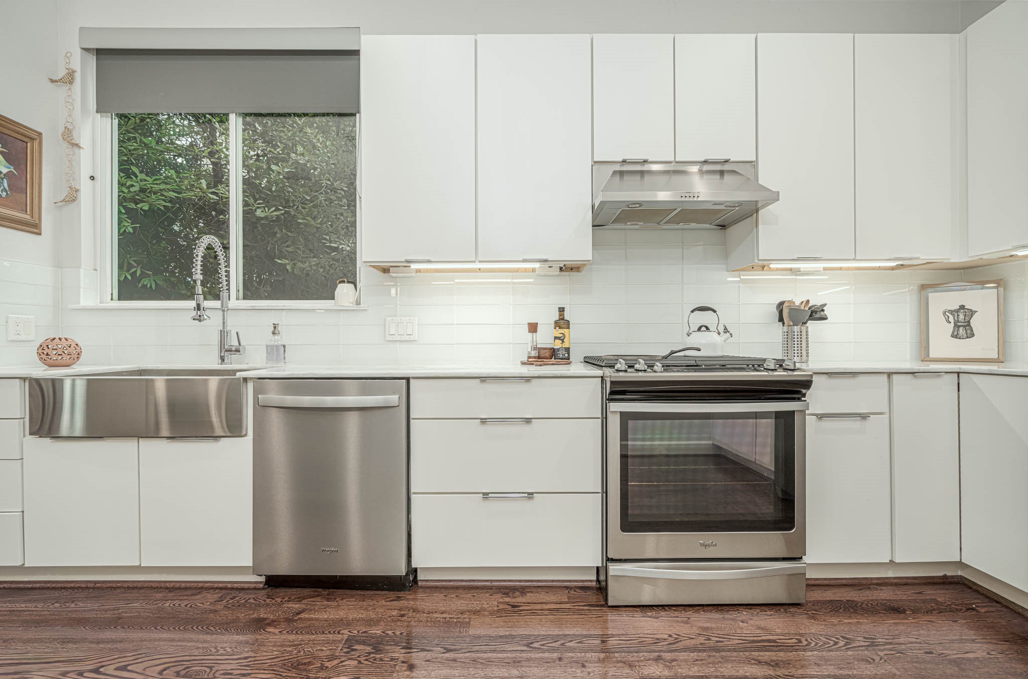 Modern kitchen featuring sleek white cabinetry, stainless steel appliances, and a stylish farmhouse sink, complemented by warm hardwood floors.