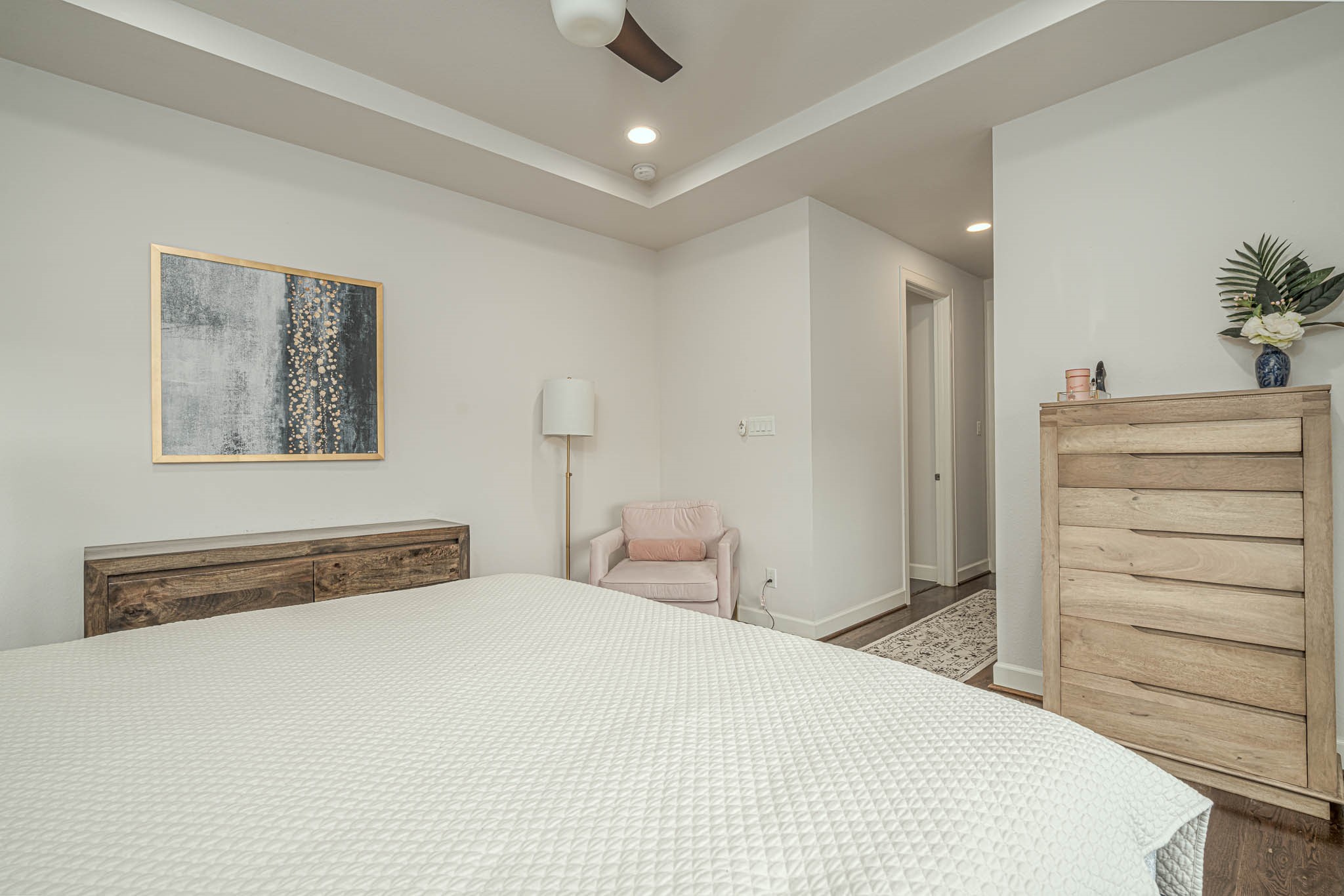 Inviting bedroom featuring a cozy layout with soft neutral tones, a stylish ceiling fan, and ample natural light. The room includes elegant wood furniture and modern decor, creating a serene and comfortable retreat.