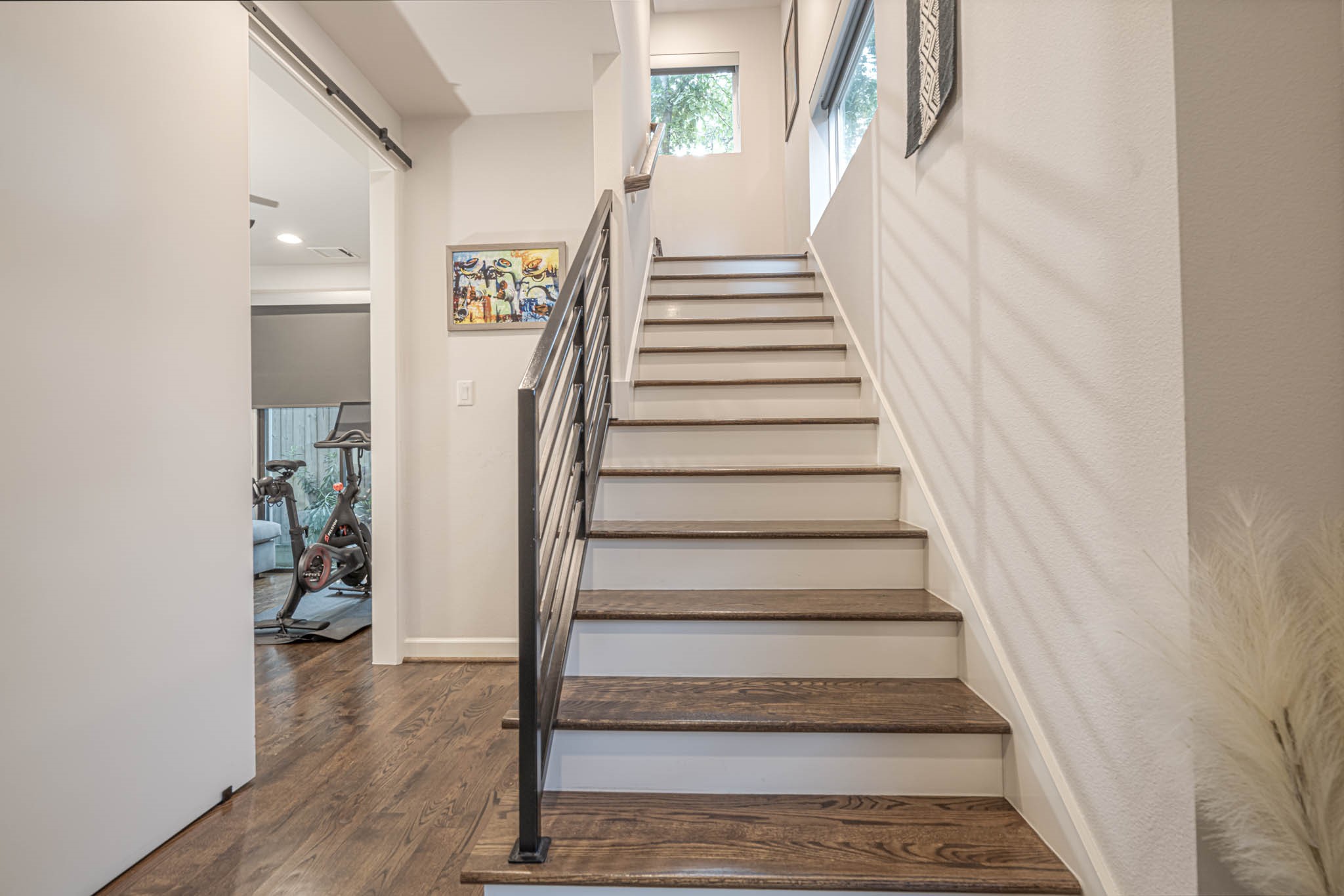 Modern staircase with sleek metal railings and wooden steps leading to a bright upper level, adjacent to a versatile room perfect for a home gym.