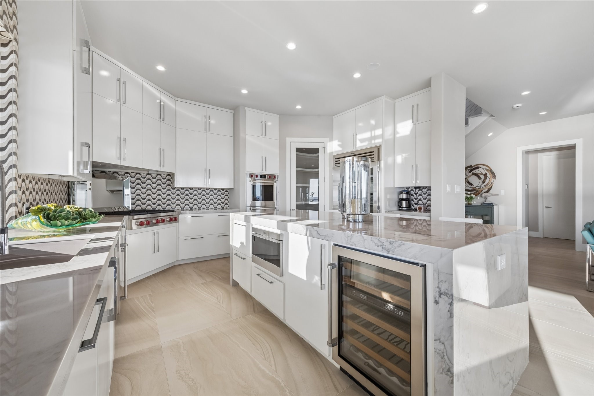 High-performance appliance package, featuring a Wolf six-burner gas cooktop, double oven, and built-in drawer microwave integrated into the island, professional Sub-Zero refrigeration with full-size fridge, freezer, ice maker, and wine fridge, and discreet Fisher & Paykel dishwashers that blend seamlessly
