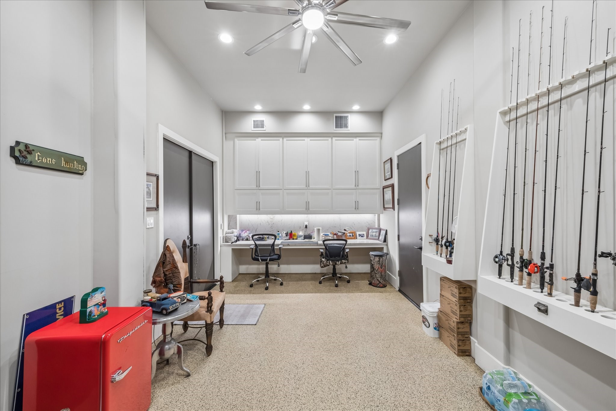 A spacious climate controlled tackle room is located on the ground level, featuring a built-in desk with an expansive workstation, abundant cabinetry for organized gear storage, and custom vertical racks designed to accommodate a large collection of fishing rods