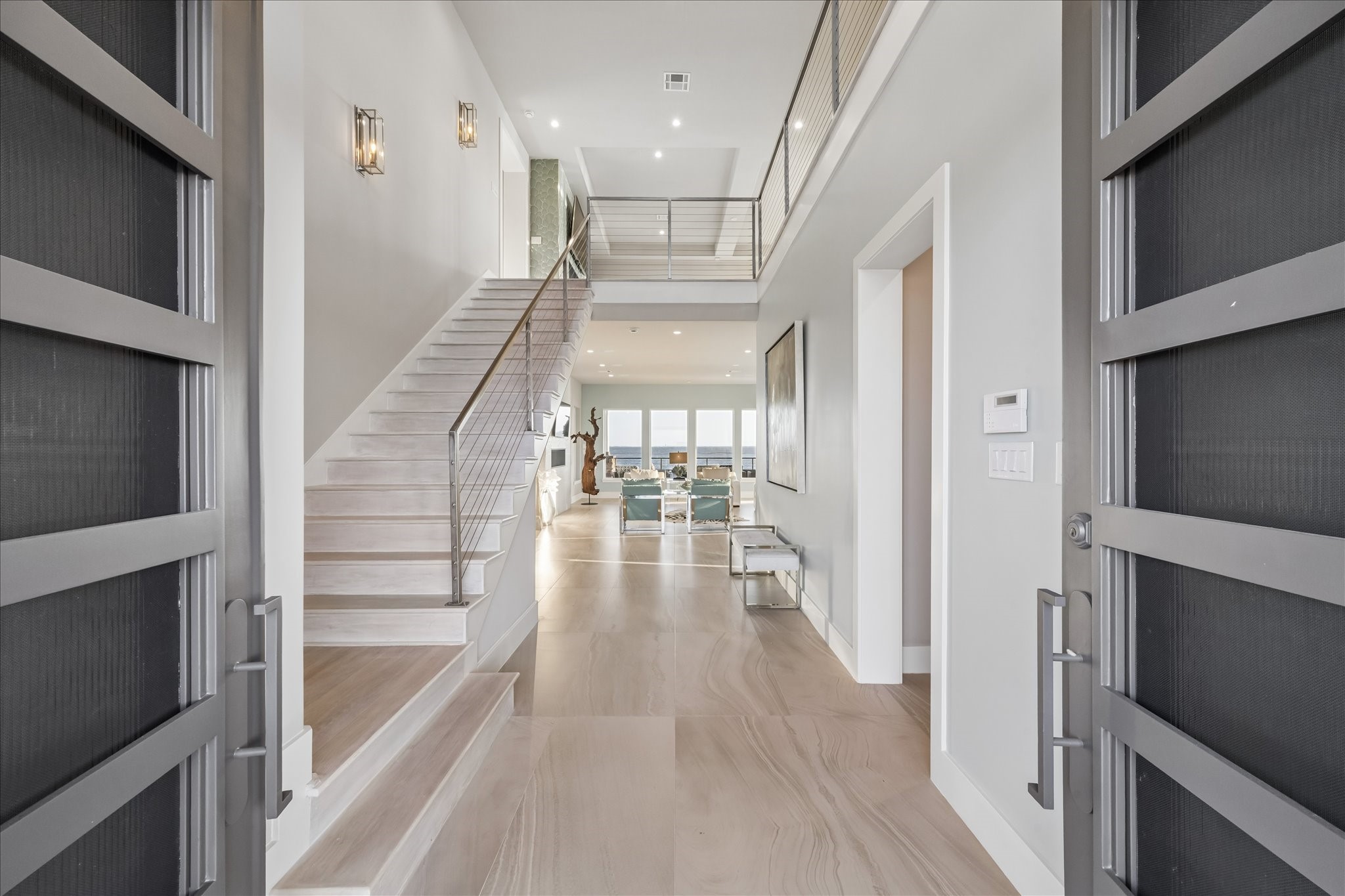 Upon entering through striking modern steel double doors, you are greeted by a light-filled foyer with soaring high ceilings and large 24" x 48" Eleganza tile flooring. The space draws your eye to the breathtaking views of West Galveston Bay, setting the tone for the homes refined, luxury design