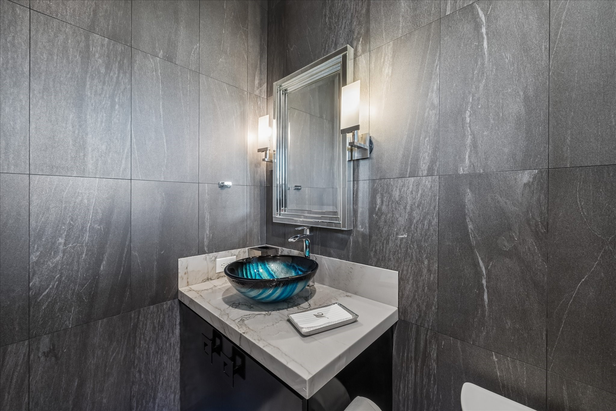 The powder room features dramatic wall tile, a stunning glass vessel sink, and quartz countertops, complemented by elegant sconces and a beautifully appointed mirror