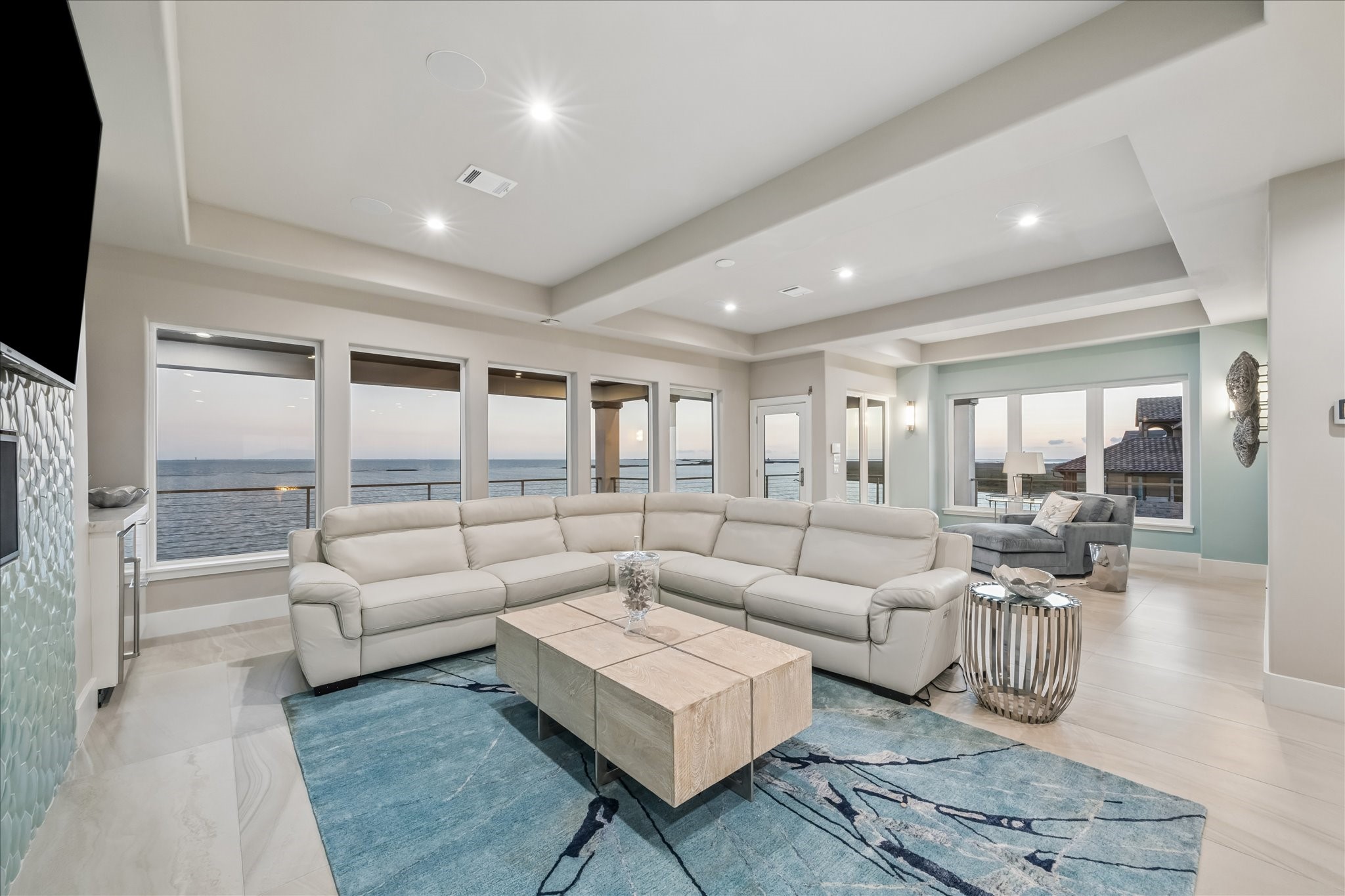 The second-level family room expands the footprint of leisure featuring a dual-zone layout with two distinct sitting areas designed to maximize the property's waterfront position. Floor-to-ceiling windows offer unobstructed views of West Galveston Bay and direct access to a private covered balcony