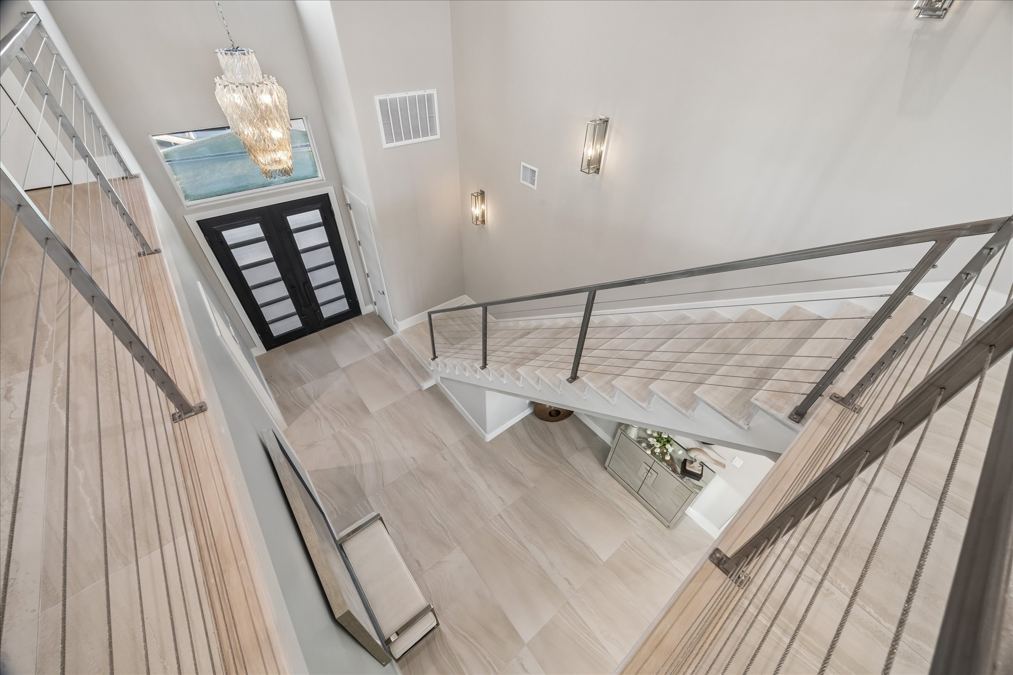 A beautiful chandelier and sleek cable-railing staircase anchor this grand, light-filled foyer, leading to the second-level living area with three additional guest bedrooms, full bathrooms, and a spacious outdoor balcony