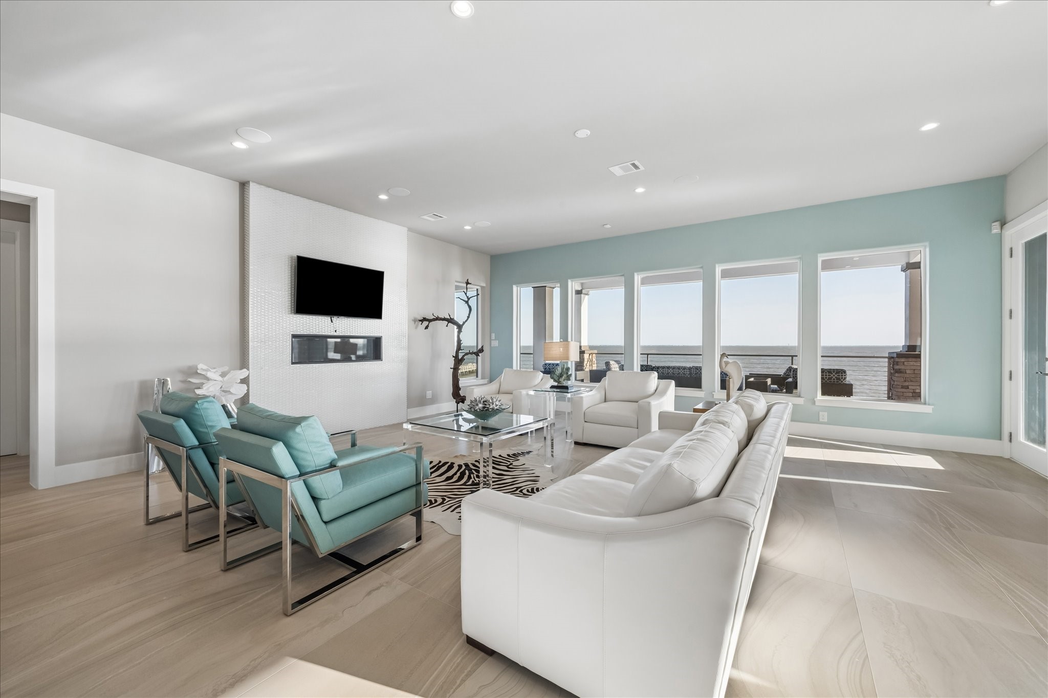 Fully furnished with a clean, coastal-inspired aesthetic, defined by its neutral palette and high-end materials. The focal point is a mosaic basket-weave tiled accent wall that seamlessly integrates a wall-mounted TV and recessed fireplace, adding architectural depth and texture to the space