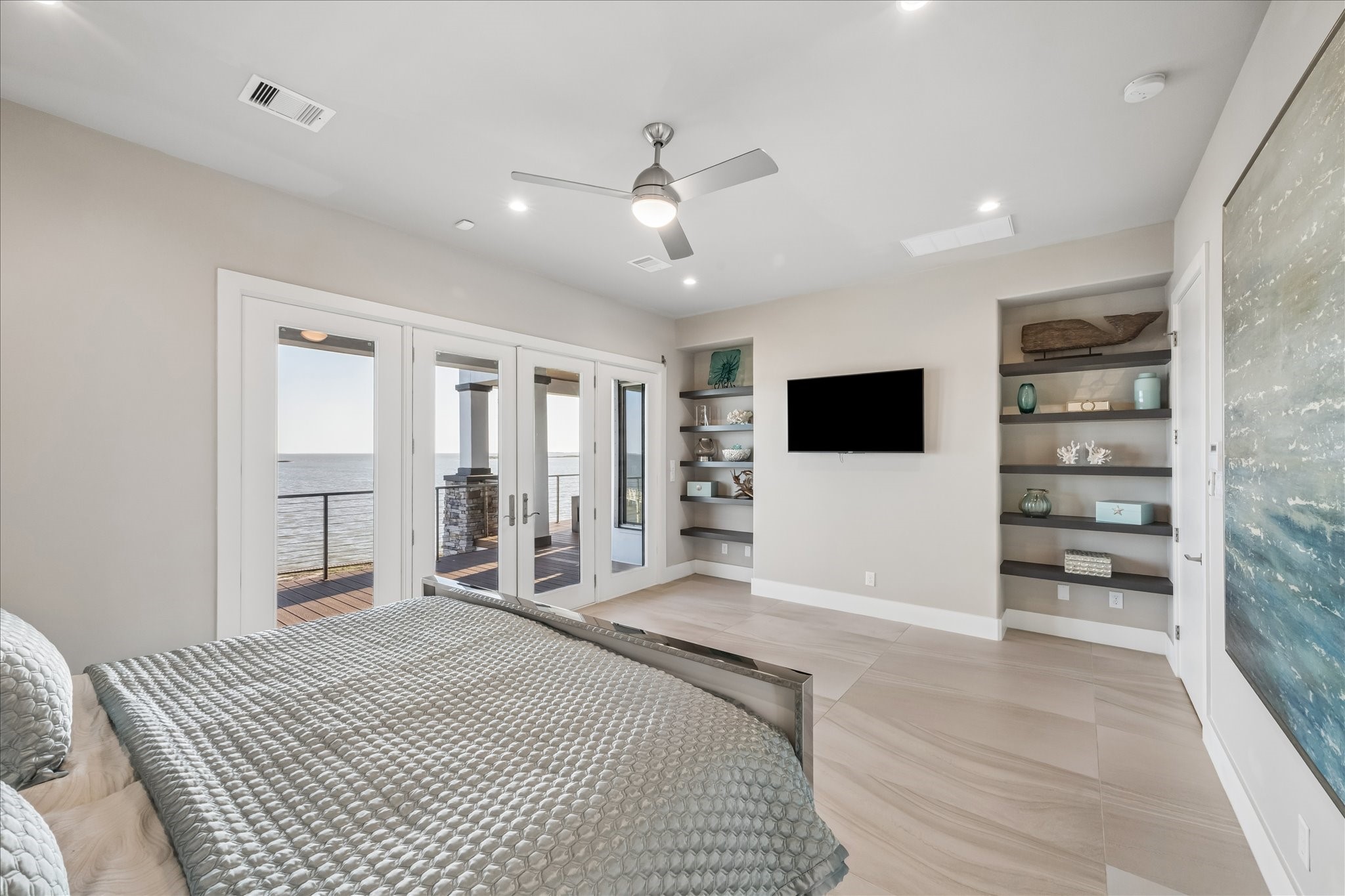 This modern primary bedroom comes fully furnished, showcasing neutral tones and open built-in shelving for stylish display and convenient storage