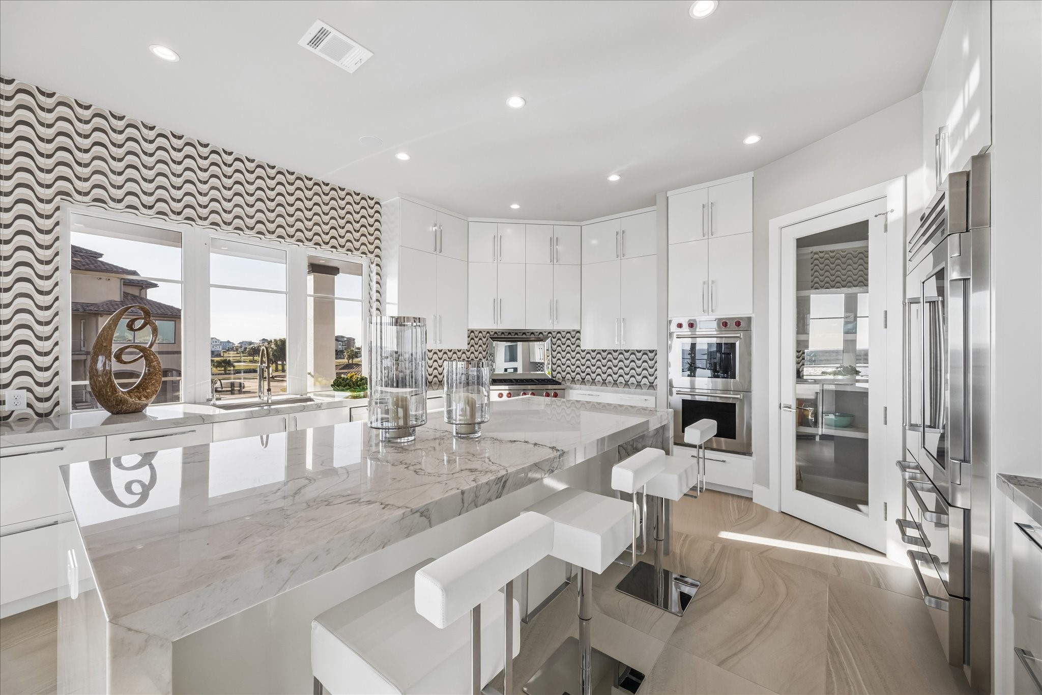 Centering the space is a large quartzite waterfall island with breakfast bar, complemented by high-gloss full-height cabinetry with full-extension, soft-close drawers, and a spacious walk-in pantry