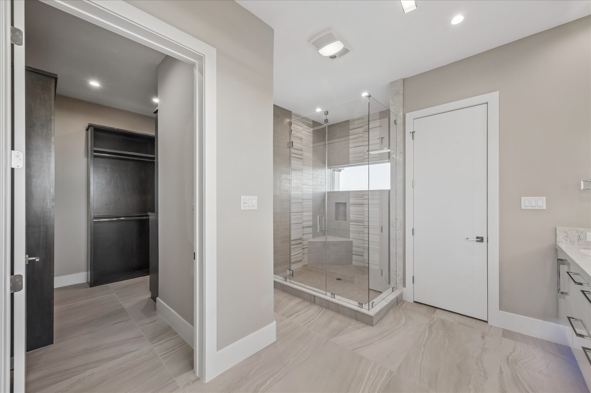To the left of the vanities there is a large walk in closet full of built-in organization and a spacious frameless walk-in shower featuring a built-in bench and a multi-jet rainfall panel