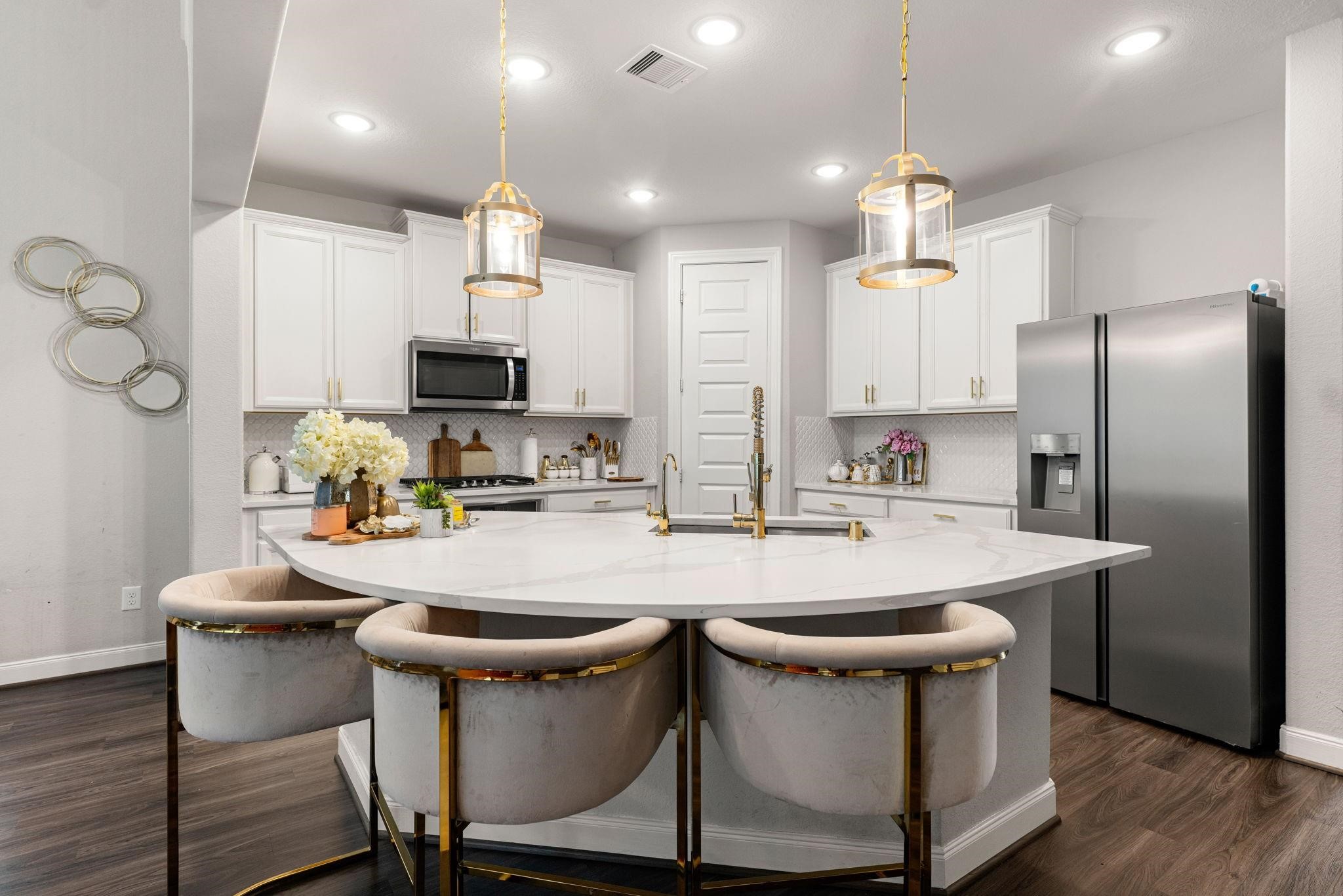 The kitchen centers around a massive curved island with bar seating, while lined with pristine white cabinetry.