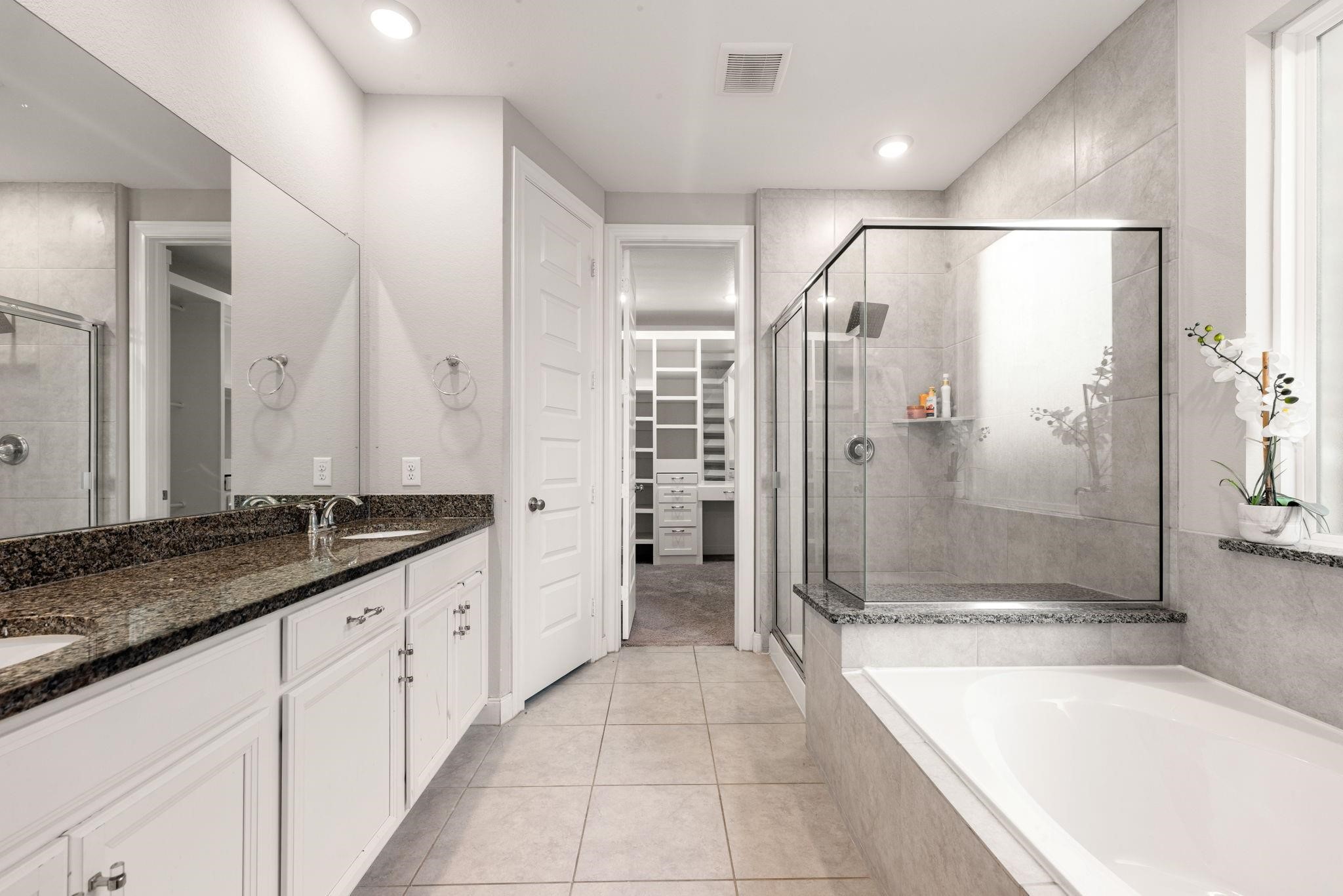 The primary bath is spa-inspired, with double sinks, a deep soaking tub, and a separate glass-enclosed shower.