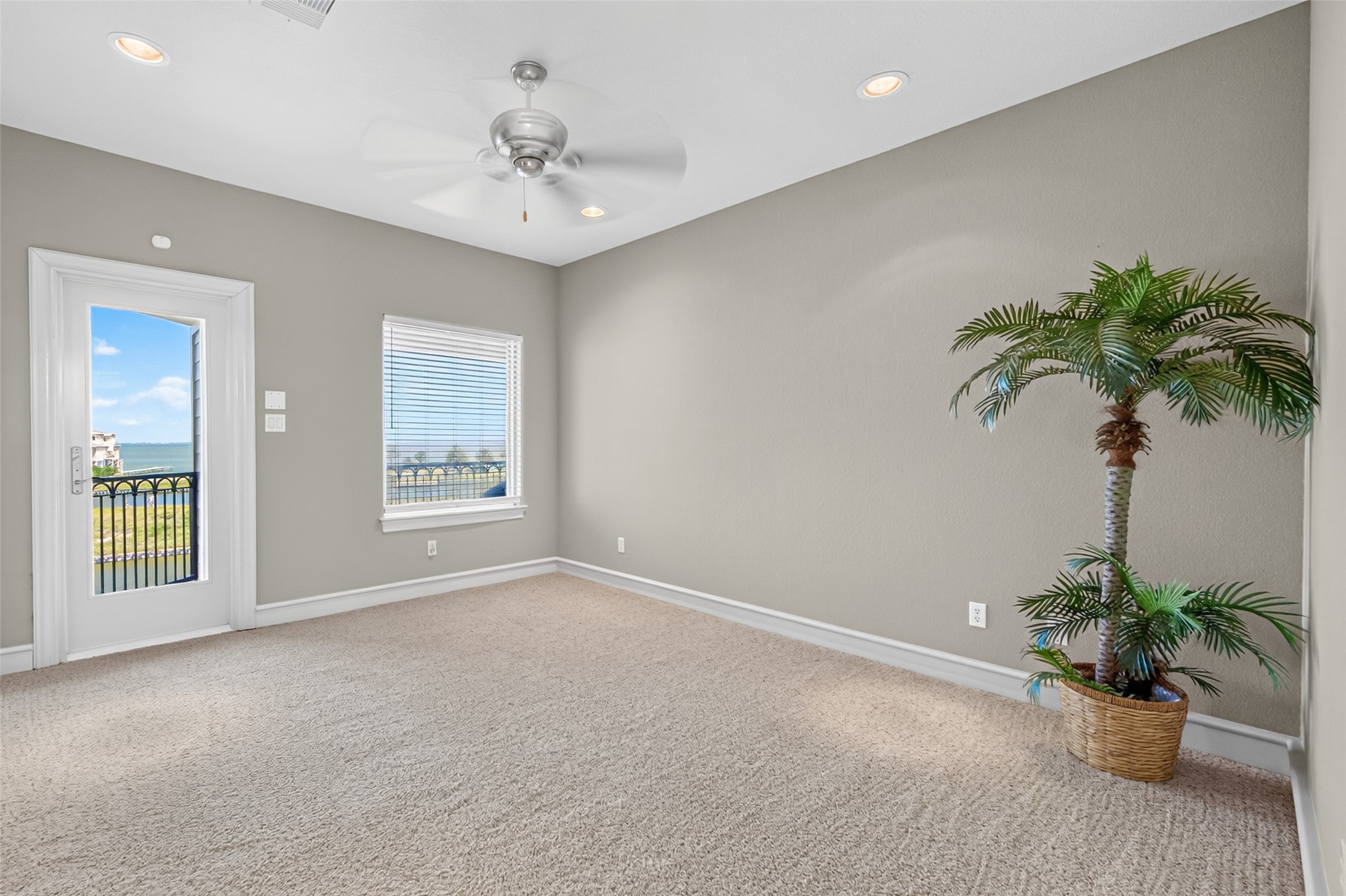 Bright, spacious room with a ceiling fan, plush carpeting, and a large window showcasing stunning outdoor views, alongside a door leading to a balcony.