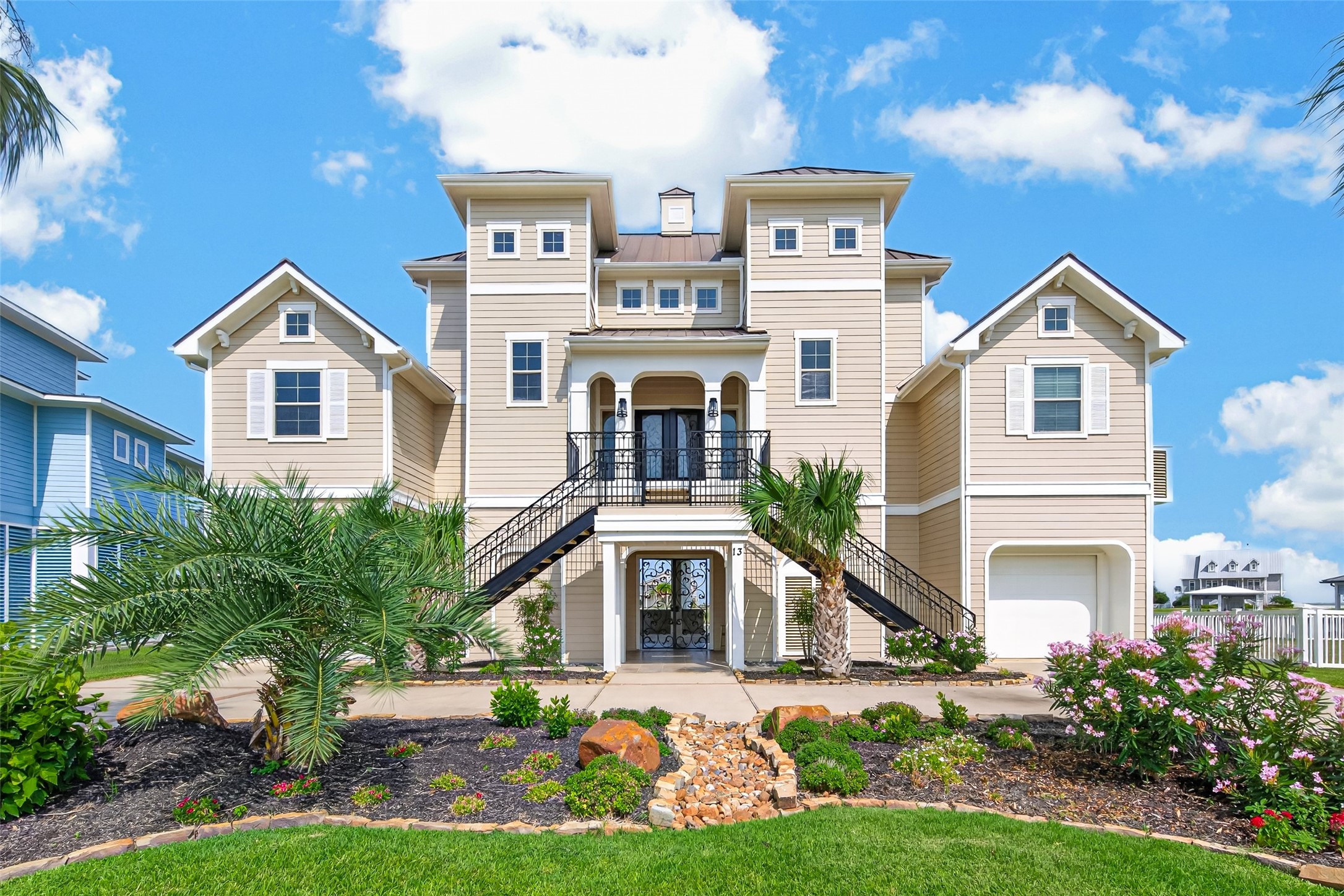 Stunning coastal home with elegant architecture, featuring dual staircases, a welcoming balcony, and lush landscaping.