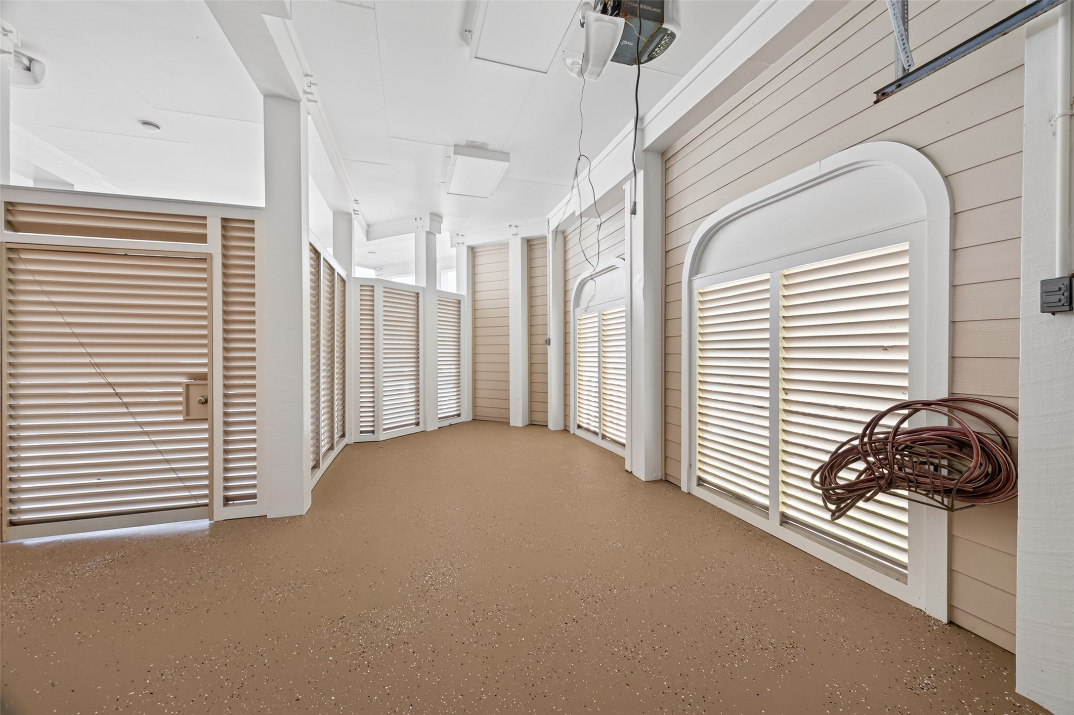 Spacious garage with clean, speckled flooring and ample natural light filtering through stylish louvered windows, perfect for storage and projects.