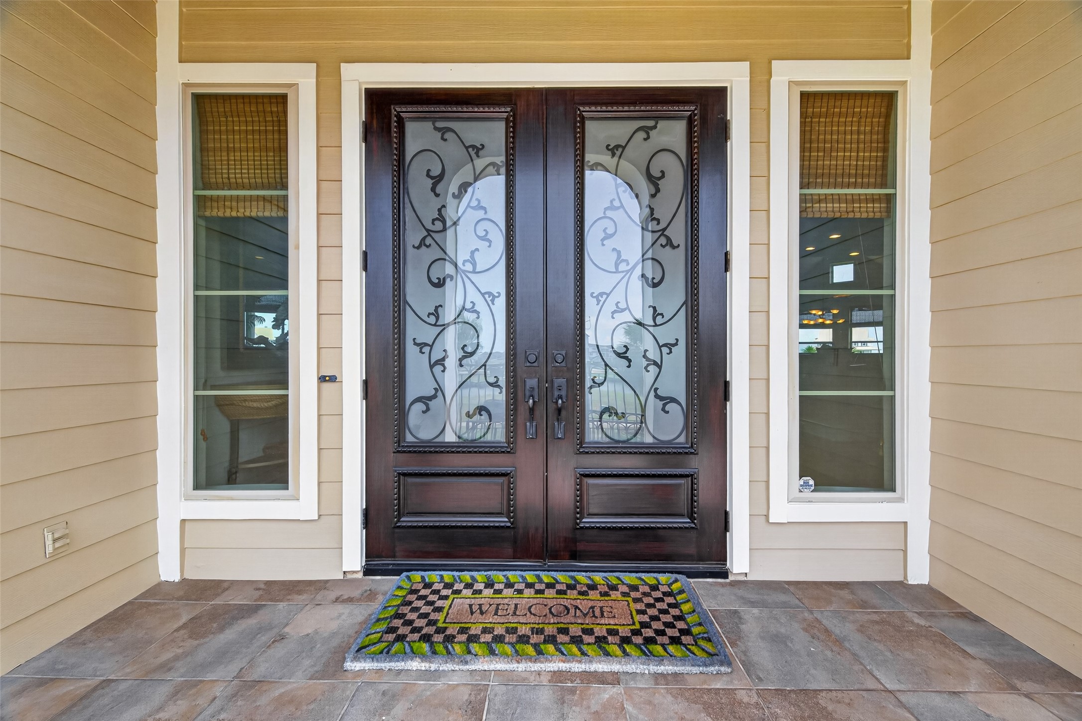 Elegant entrance featuring a beautifully crafted double door with intricate glass detailing, flanked by tall windows and a welcoming mat.