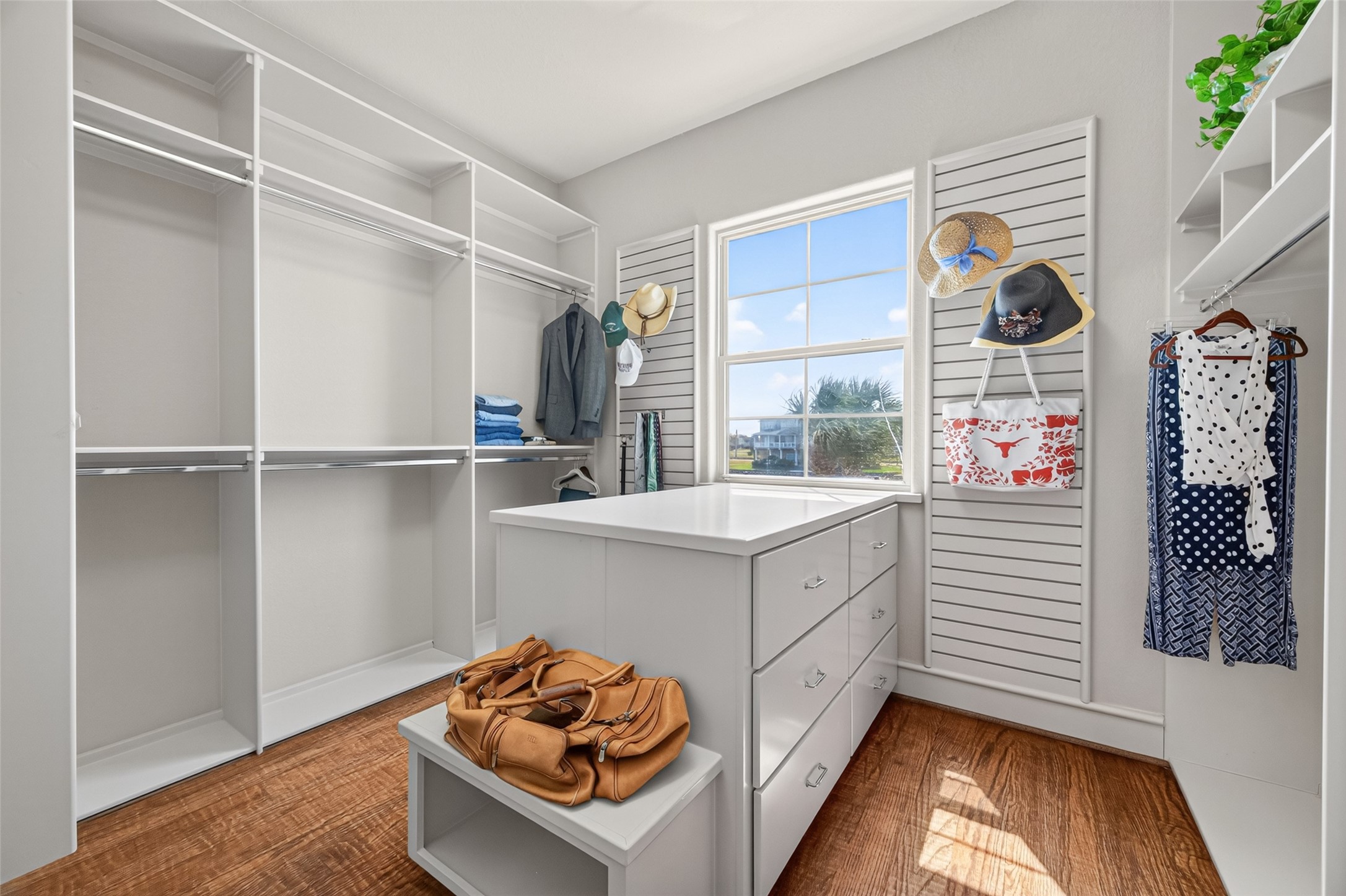 Spacious walk-in closet featuring ample shelving and hanging space, an island with drawers, and a bright window for natural light.