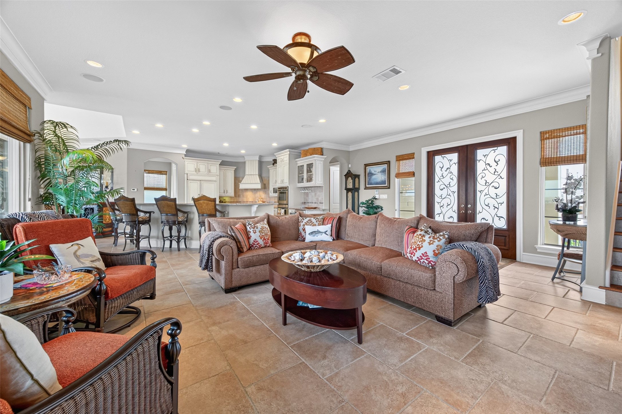 Spacious open-concept living area featuring a cozy sectional, elegant ceiling fan, and abundant natural light, seamlessly flowing into a modern kitchen with a breakfast bar and stylish cabinetry.