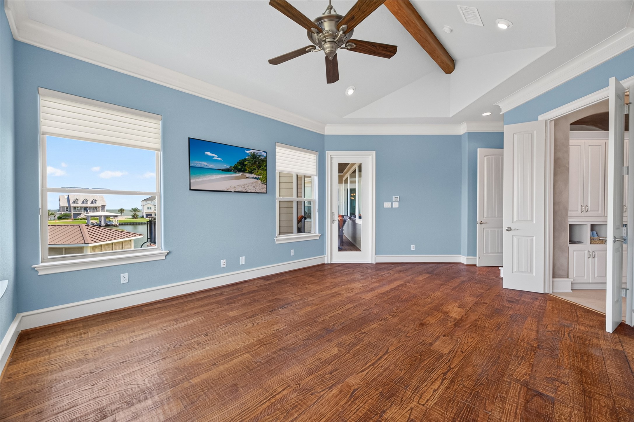 Spacious room with elegant hardwood floors, vaulted ceiling with wooden beams, and abundant natural light from large windows.